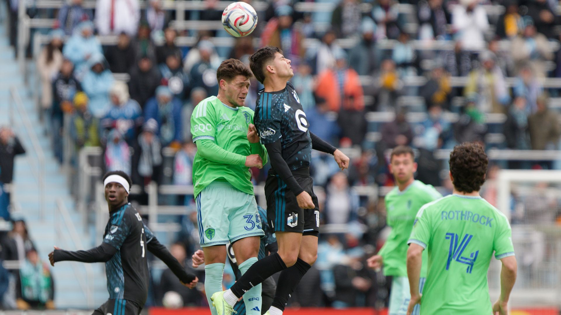 Soccer players go head to head for a ball as they leap into the air. 