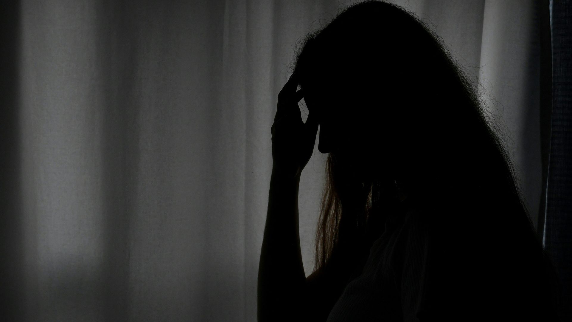 A shadowy picture of a girl with her hand to her face