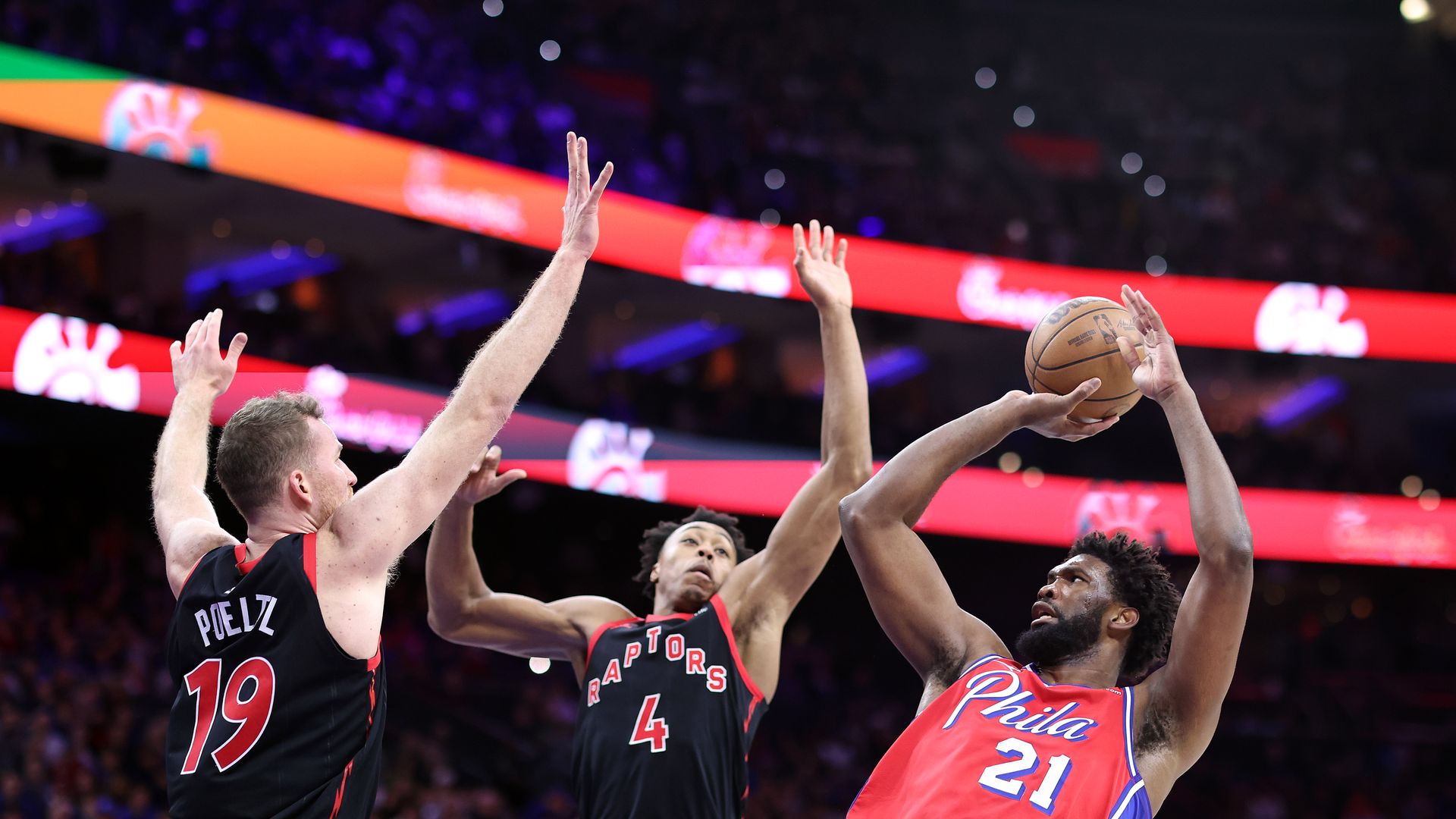 Sixers' star Joel Embiid shoots over two Toronto Raptors defenders.