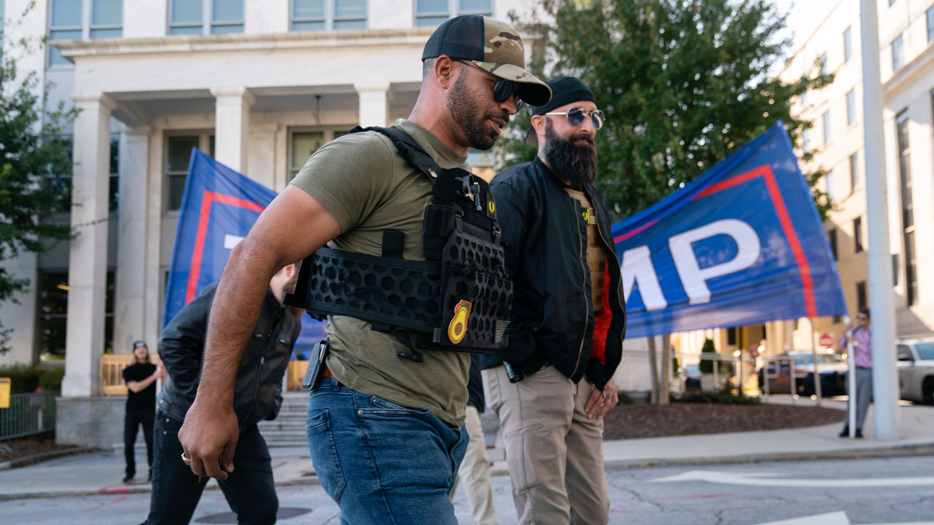 Photo of Enrique Tarrio walking on a street with a Trump banner waving behind him