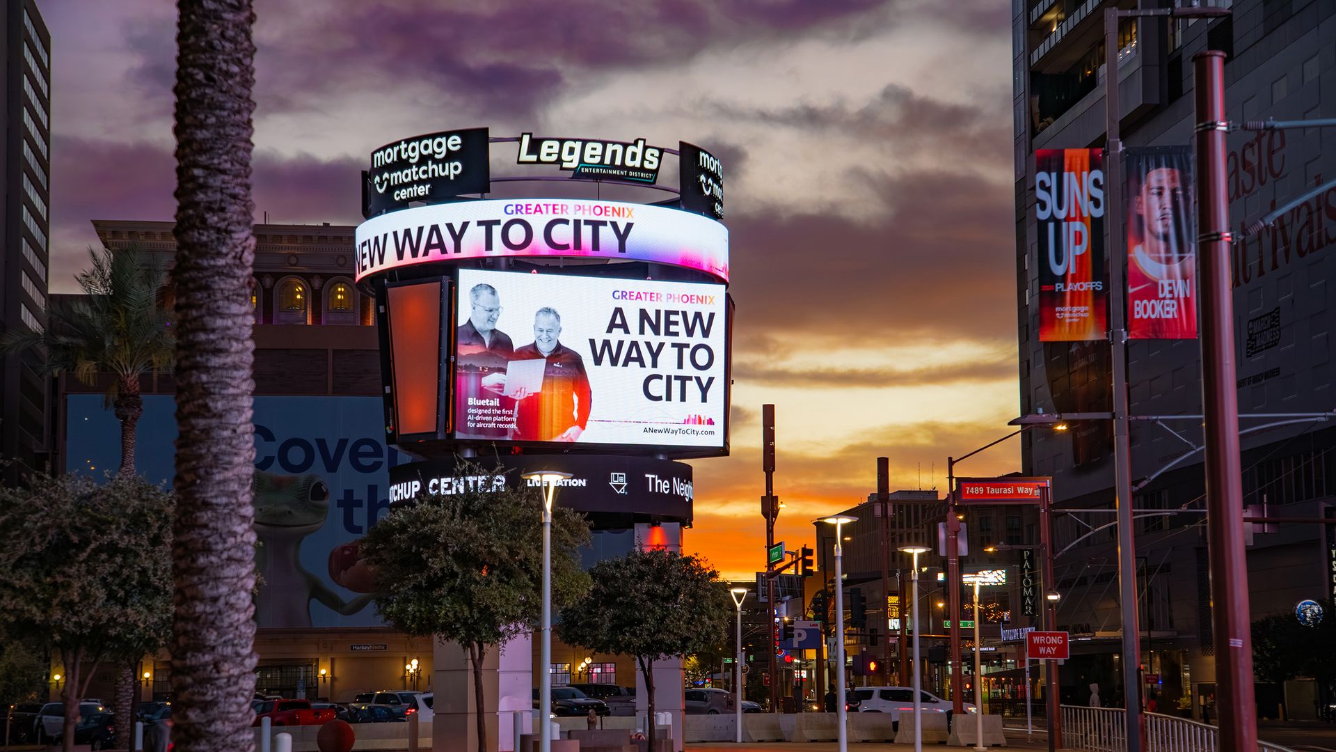 Sunset street scene with a large circular digital billboard reading A NEW WAY TO CITY; a Legends sign above, palm trees in the foreground, and a building with red banners on the right.