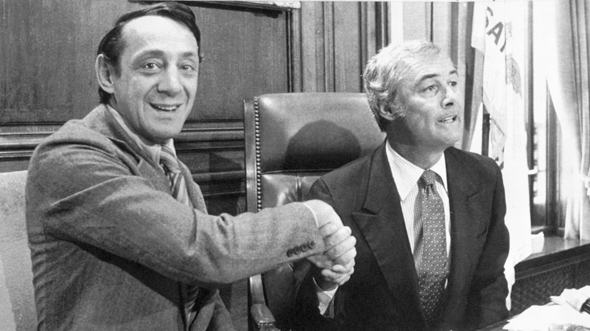 black and white photo of harvey milk and george moscone wearing suits, shaking hands