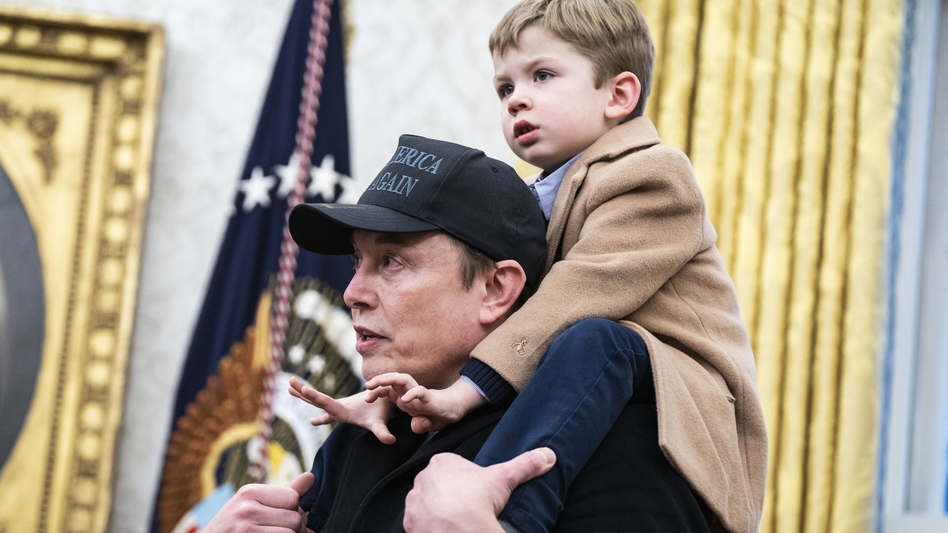 A photo showing Elon Musk in the Oval Office with his young son on his shoulders.