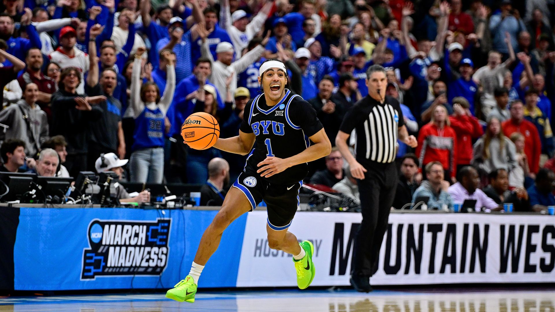 A man in a black basketball uniform dribbles and looks happy