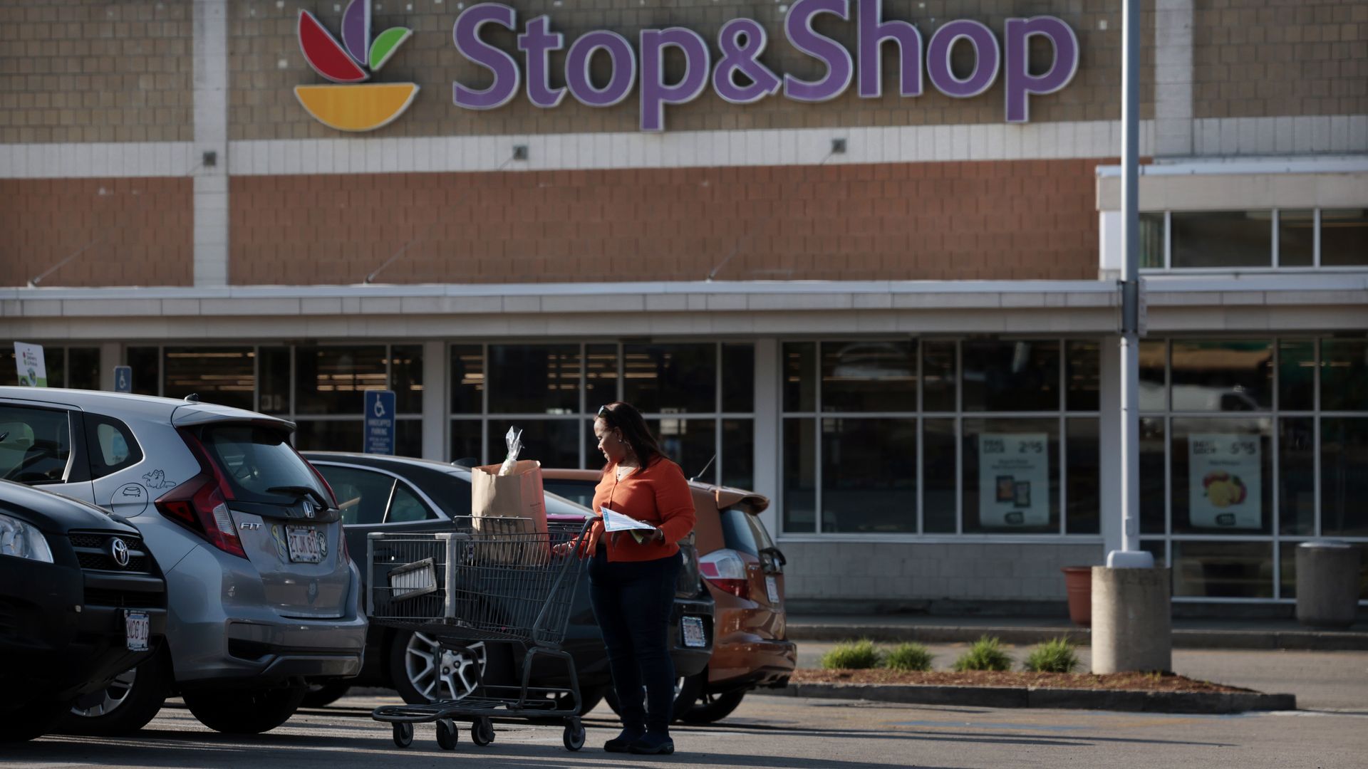A woman rolls a cart with a bag of groceries to a car outside the Stop & Shop in Boston's Jamaica Plain neighborhood.