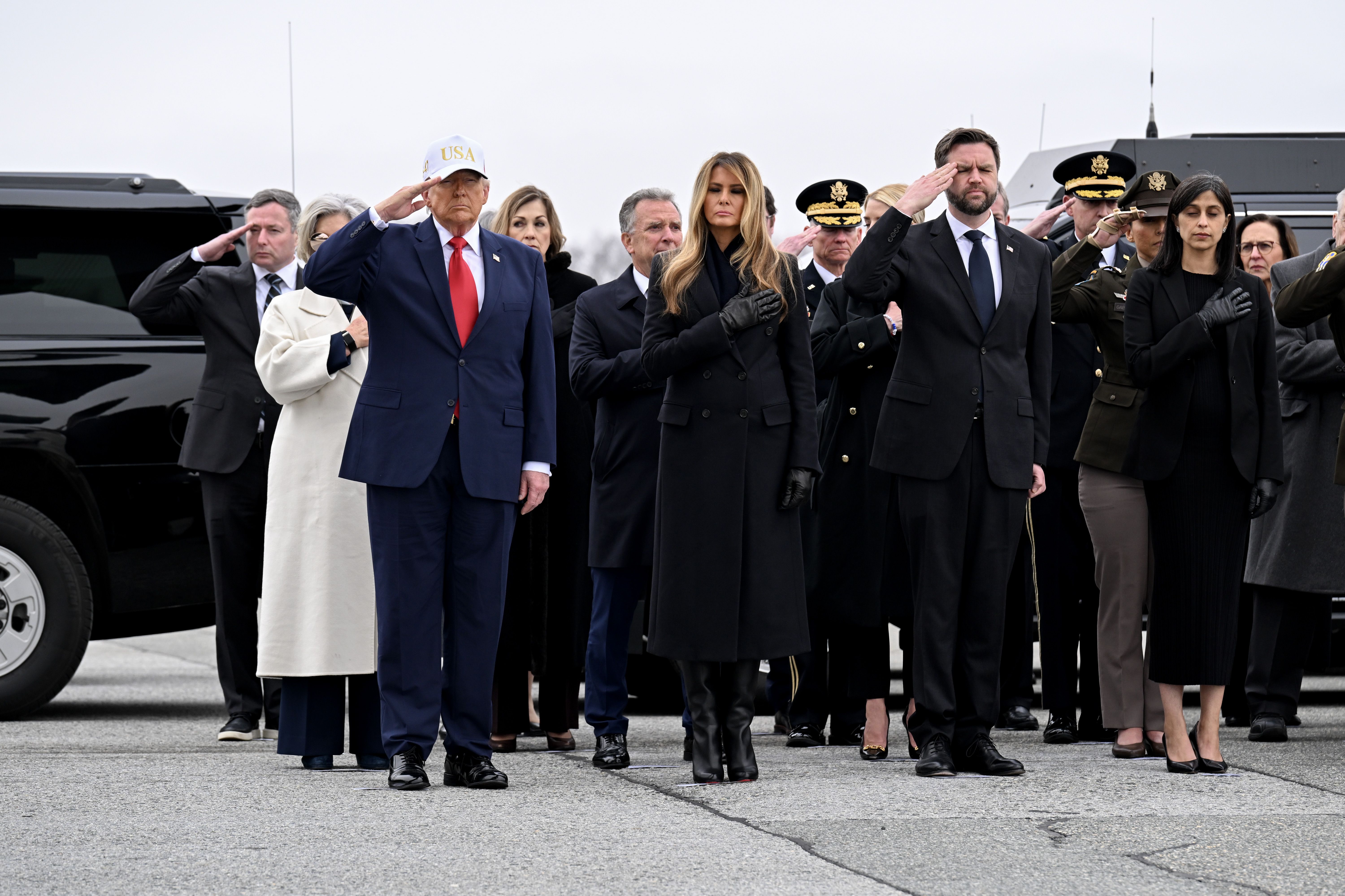 : U.S. President Donald Trump, first lady Melania Trump, Vice President JD Vance, and second lady Usha Vance stand at attention as a U.S. Army carry team moves a flag-draped transfer case at Dover Air Force Base March 07, 2026 in Dover, Delaware. Six soldiers from the 103rd Sustainment Command were 