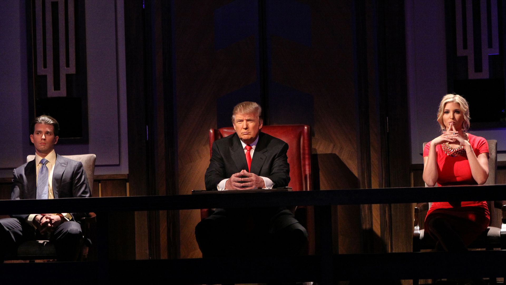 Donald Trump, Donald Trump Jr. and Ivanka Trump sit at a desk during the Celebrity Apprentice live season finale.