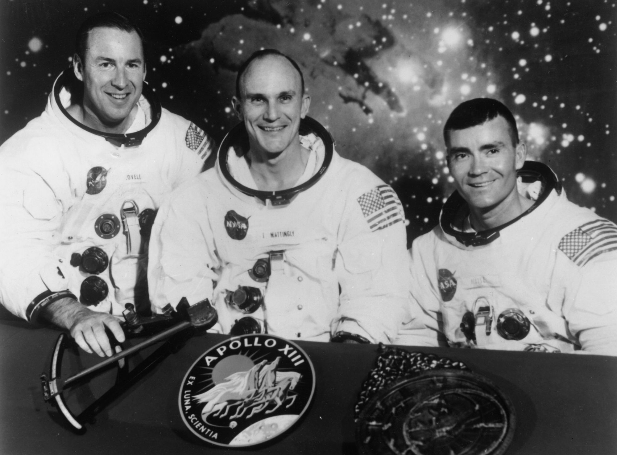 Black and white image of three astronauts in their uniforms, smiling with what looks like outer space behind them.