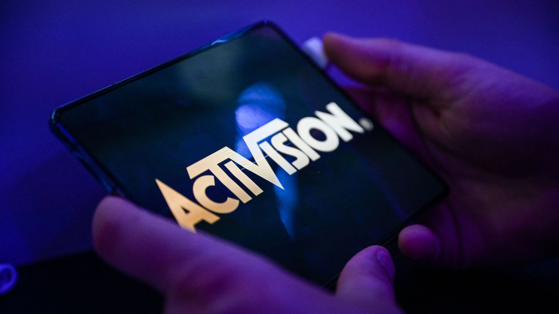 Close-up photo of a person's hands as they hold a phone that displays the Activision logo