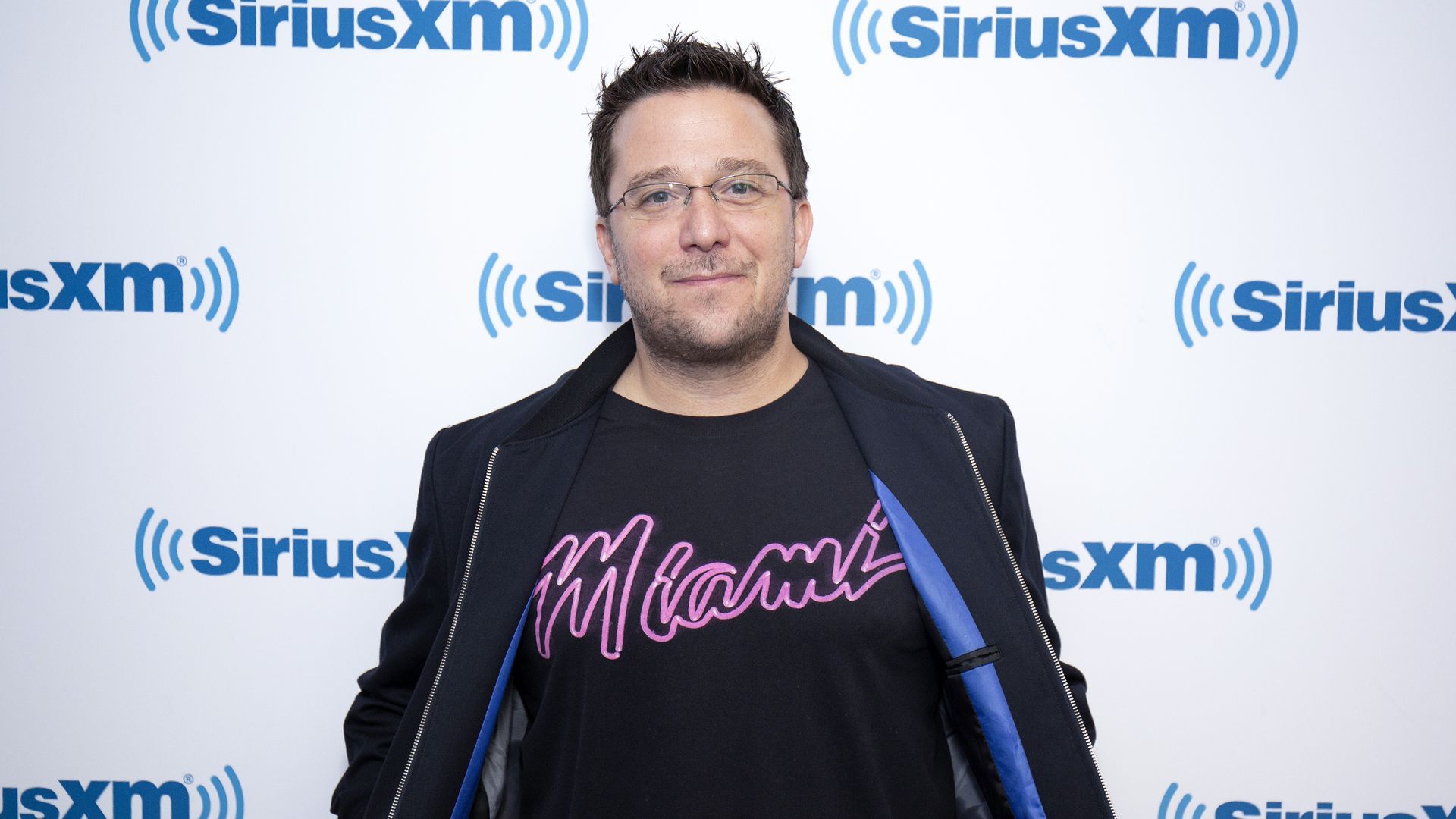 Billy Corben poses wearing a black T-shirt that says Miami.