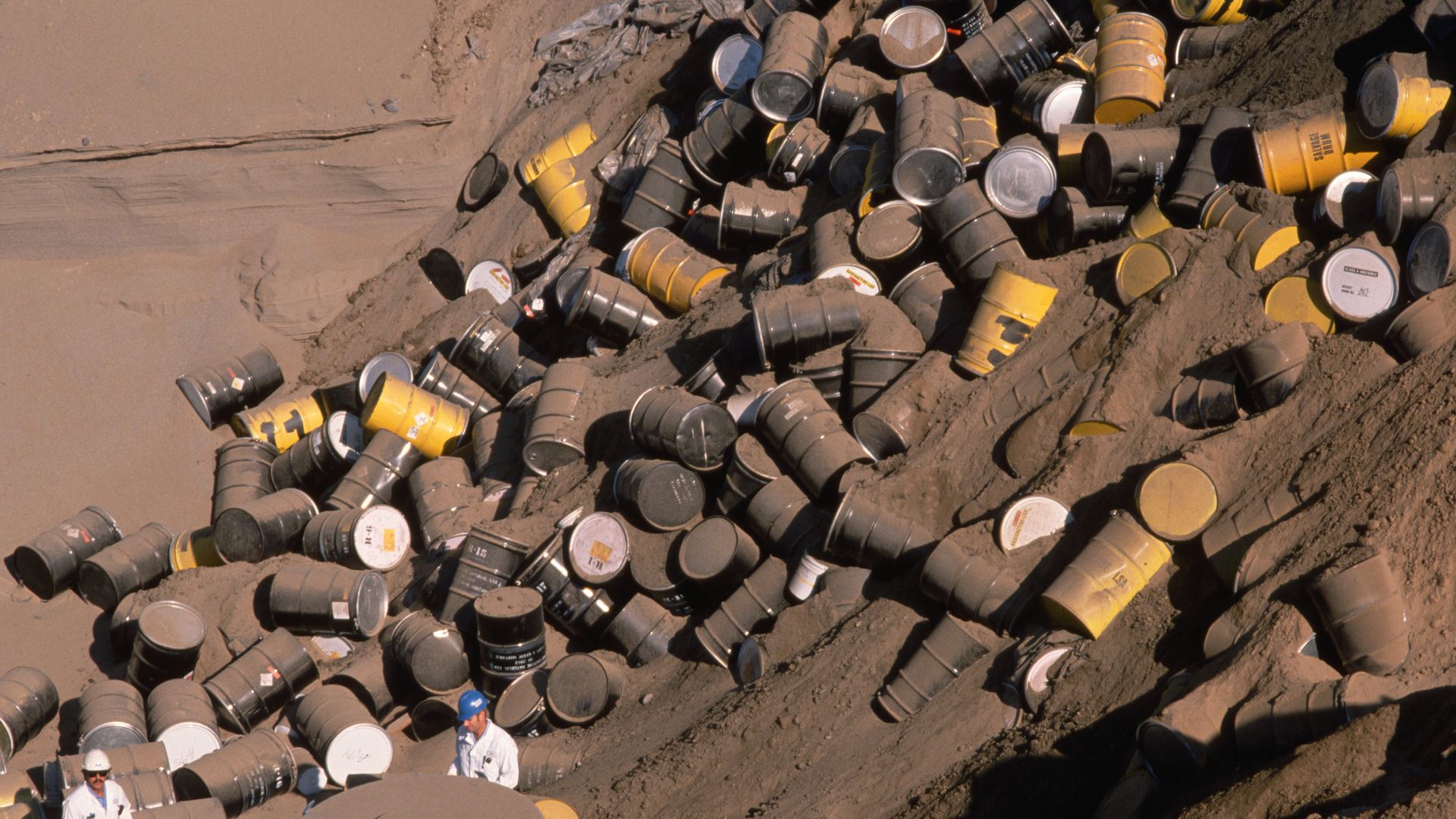 A person stands next to a huge mound of barrels containing nuclear waste. 