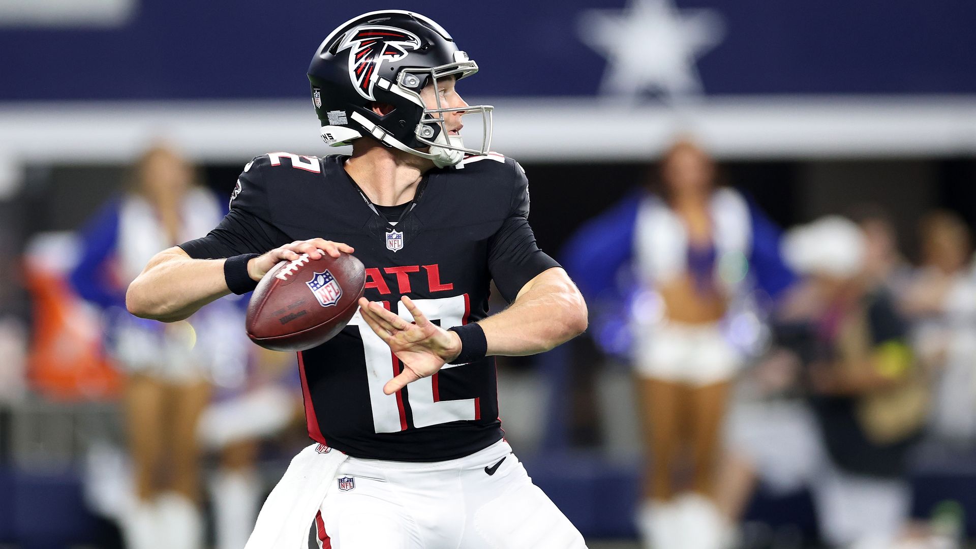 An Atlanta Falcons football player wearing a helmet and black jersey with red and white lettering prepares to throw a football. 