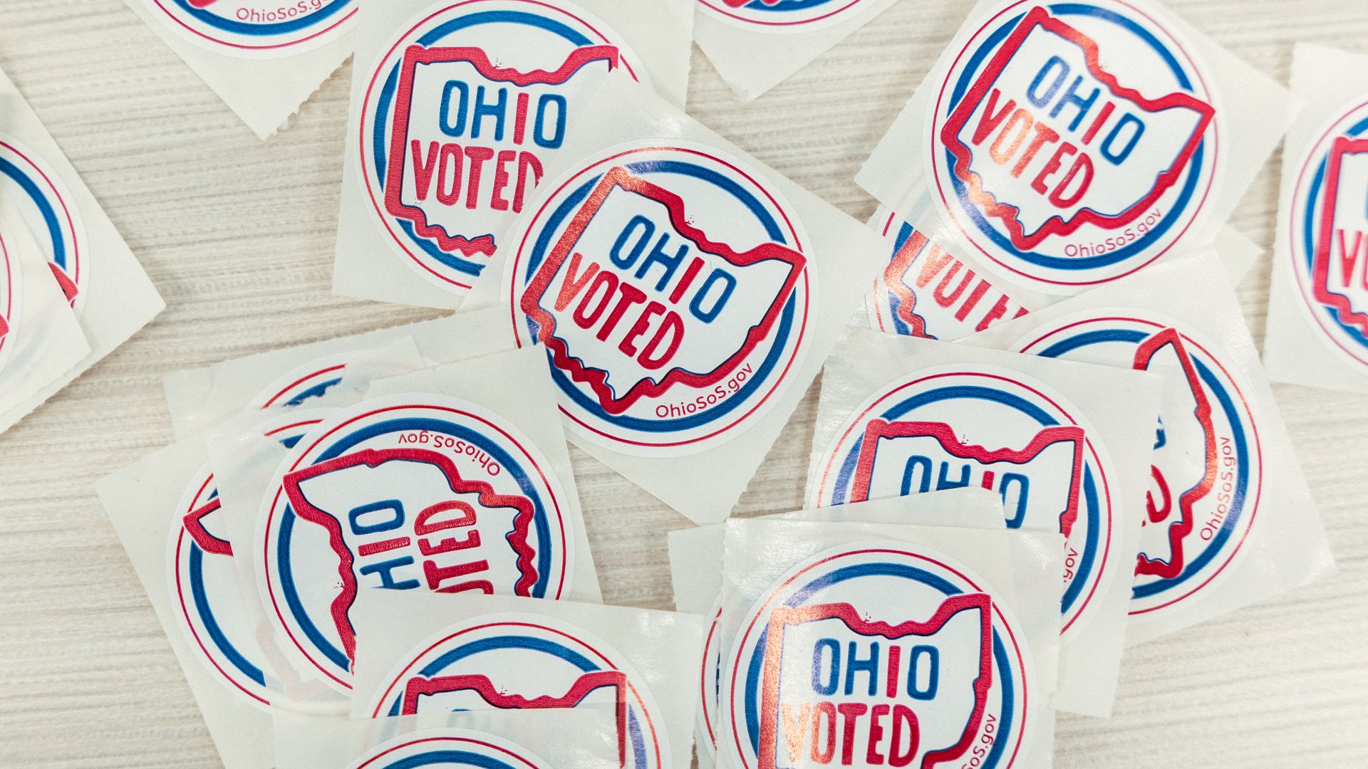 Several circular stickers say "OHIO VOTED" in blue and red, featuring the state's outline; they are scattered on a light wooden surface with white backing.