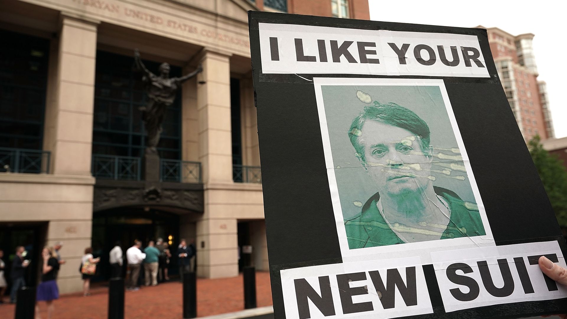 An activist holds a sign with a photo of Paul Manafort's mug shot, that reads: "I like your new suit."