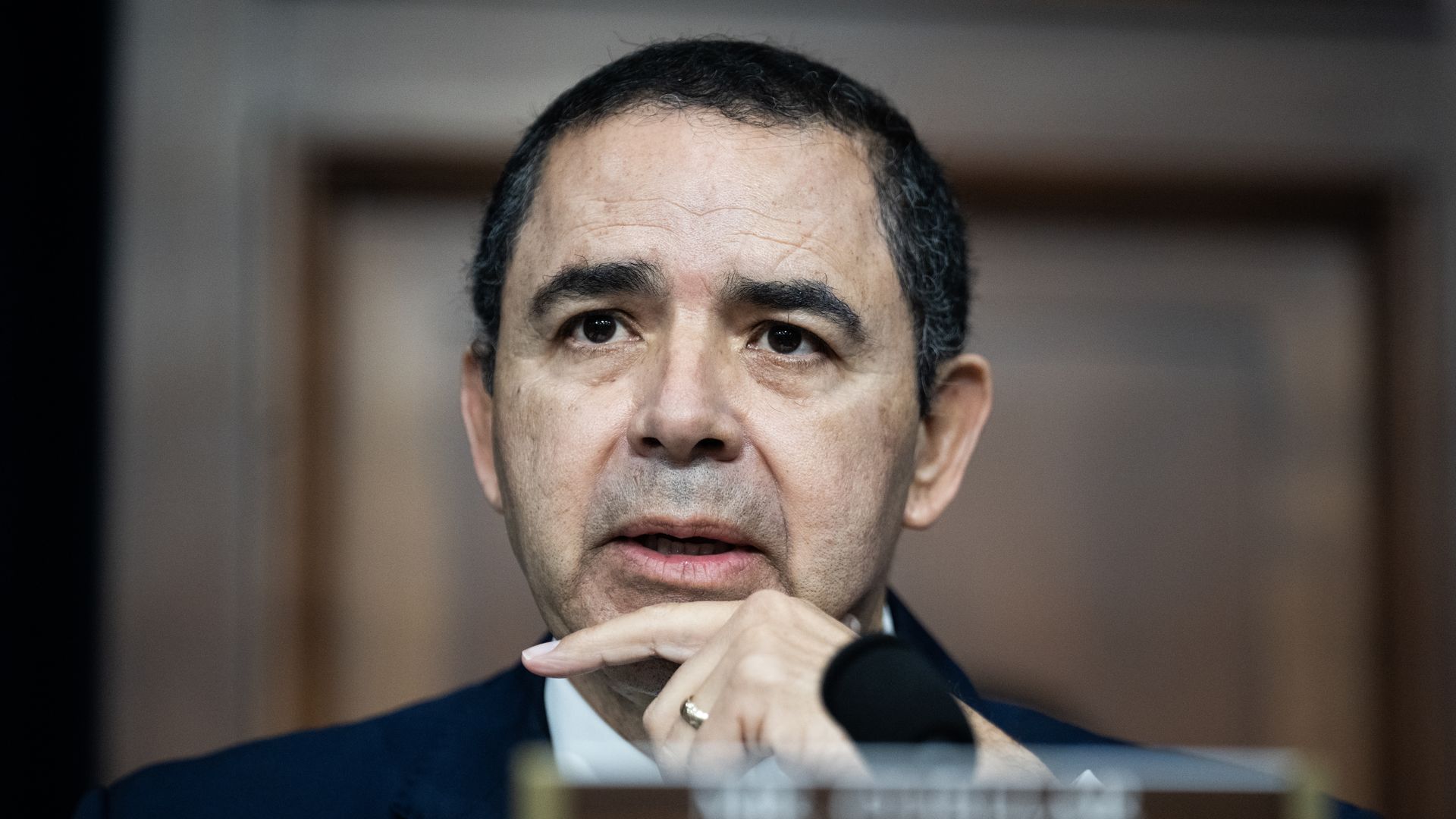 Henry Cuellar holds his hand to his chin during a congressional hearing as he speaks into a microphone.