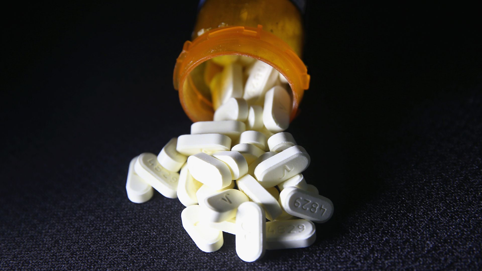 An amber drug vial with white painkiller pills falling out.
