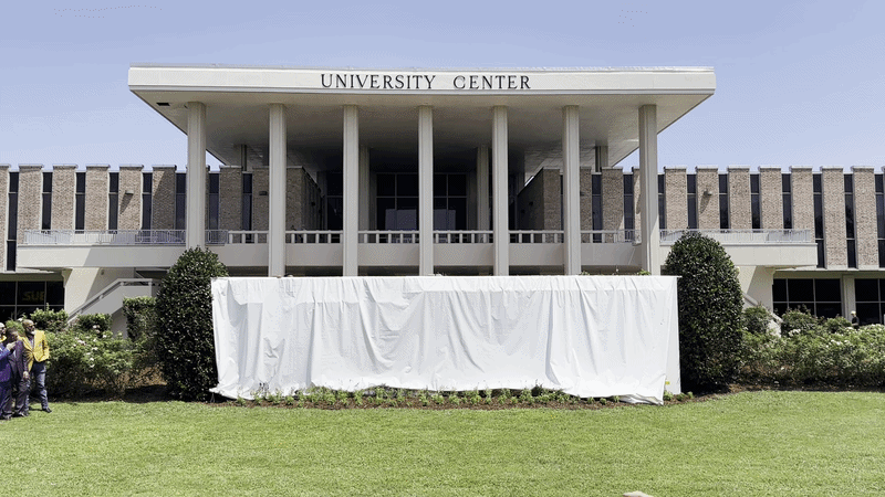 A large white banner drops to reveal a sign that says "LSU New Orleans: Home of the Privateers" in front of a building with its own sign reading "University Center."
