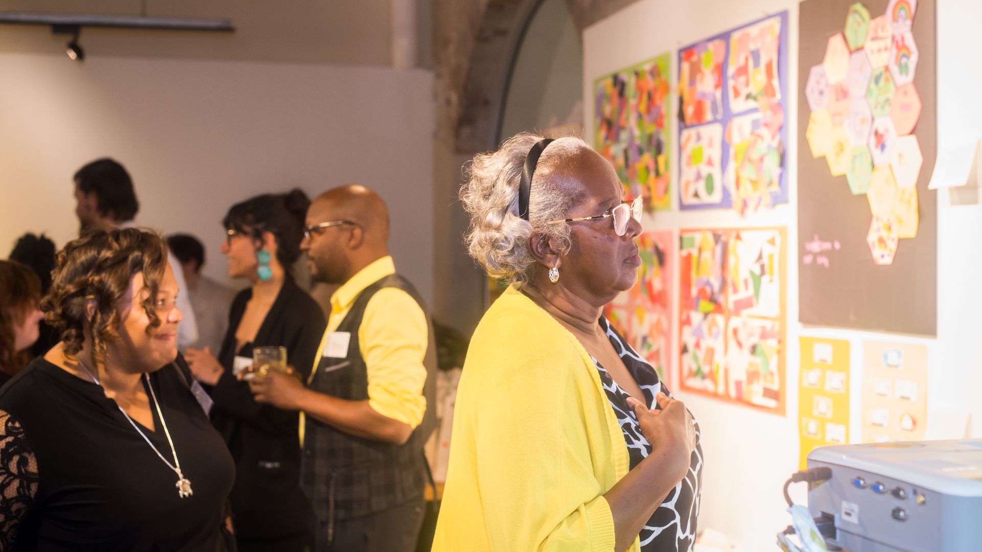 Two women browse art on a gallery wall during a cocktail event. 