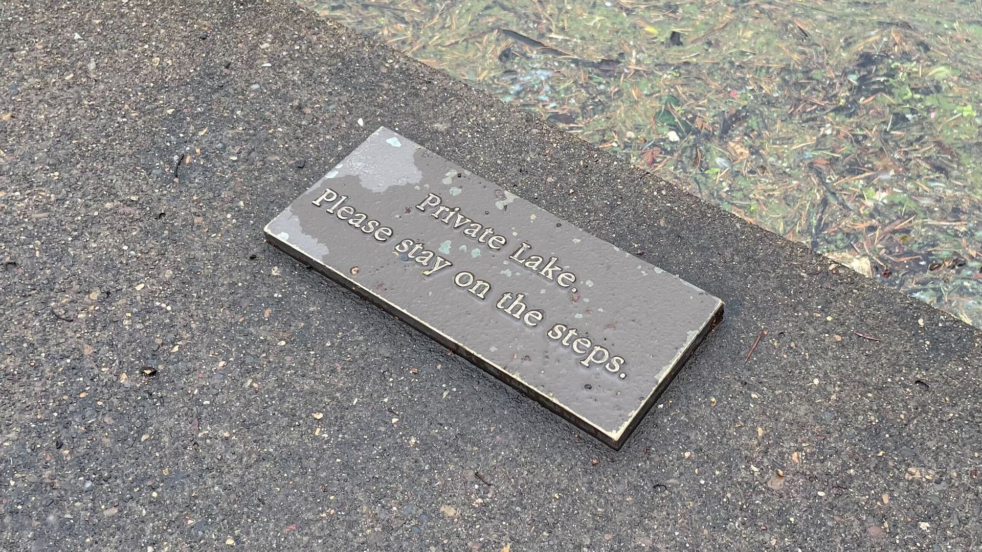 A plaque affixed to the ground reads "Private lake. Please stay on the steps."