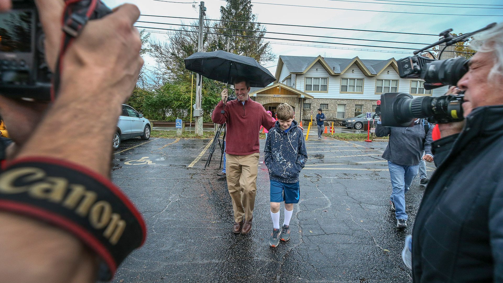 In this image, Beshear walks with one arm on his son as he carries an umbrella.