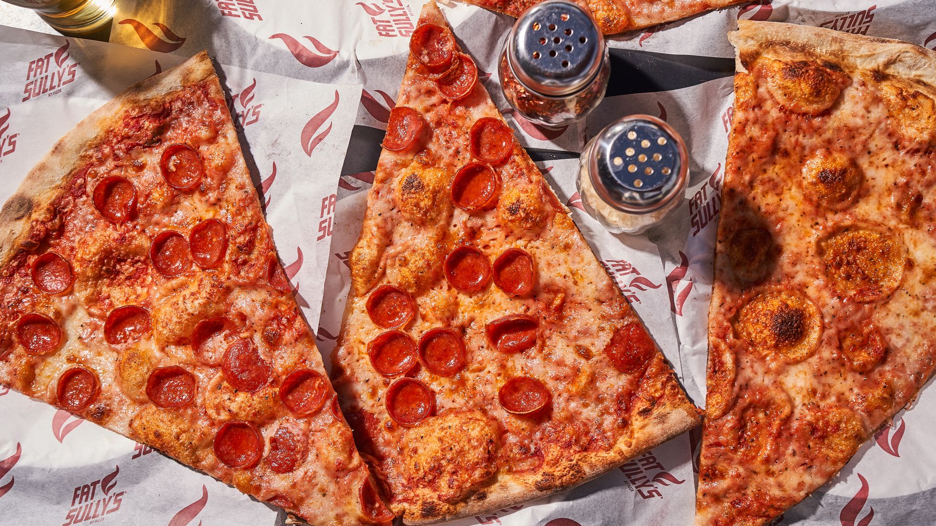 Slices of large, cheesy pepperoni pizzas on a table.