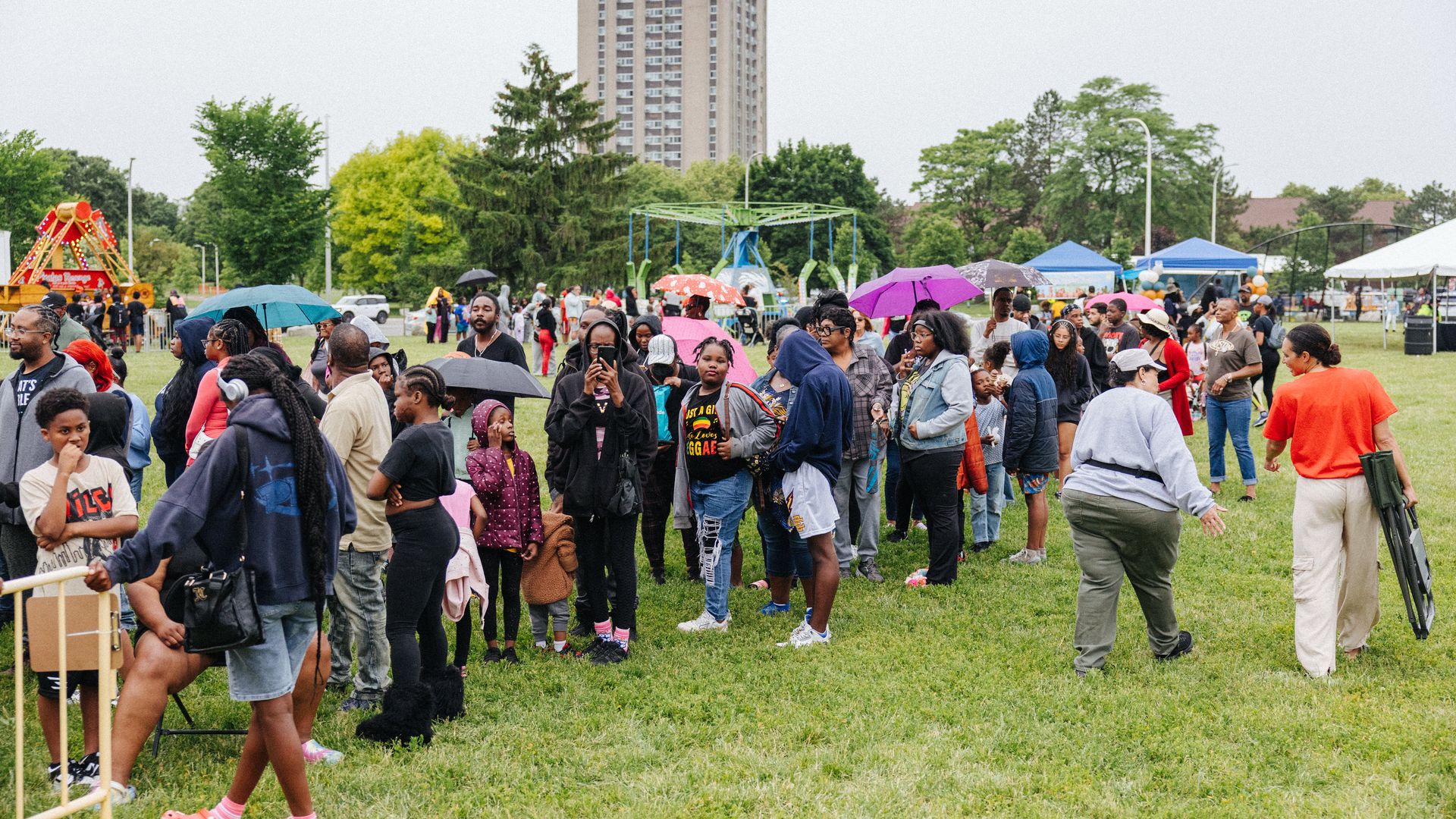 Kids and adults wait in line, with carnival rides and tents in the background