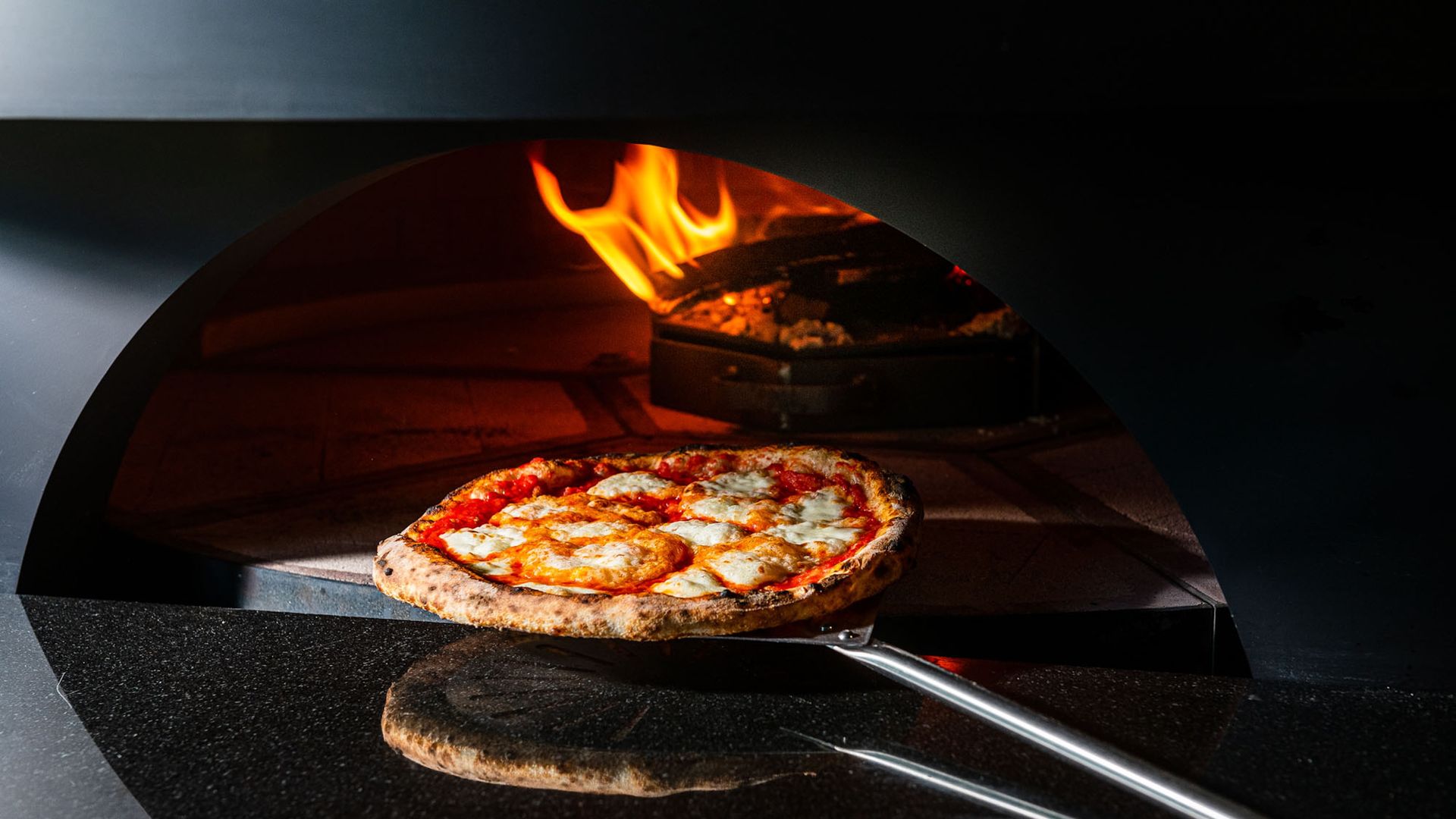 A Neapolitan pizza with red sauce and white cheese coming out of an oven with a wood fire in the background.