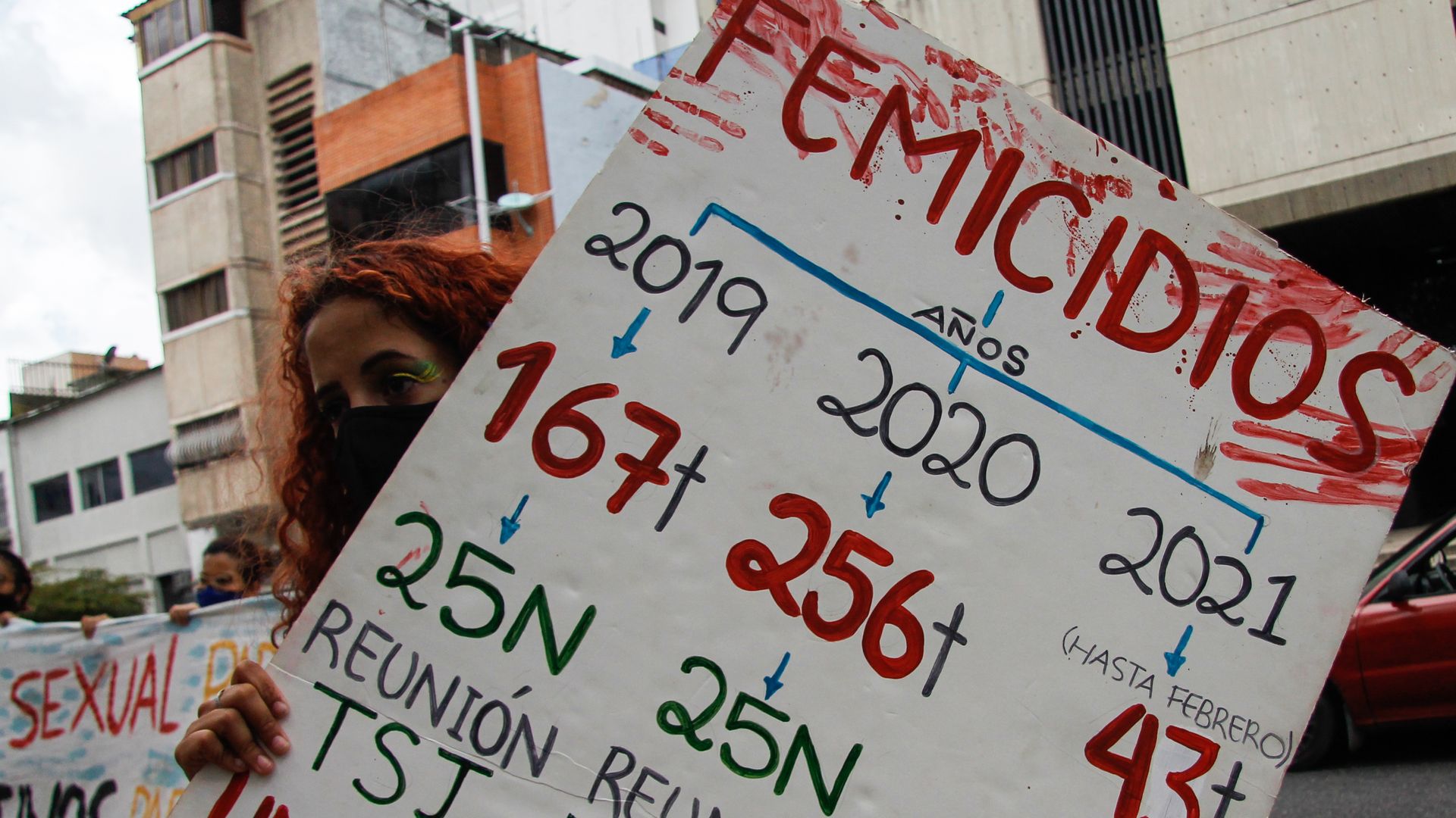 Photo of a woman holding a sign that indicates the number of femicides in Venezuela in Spanish