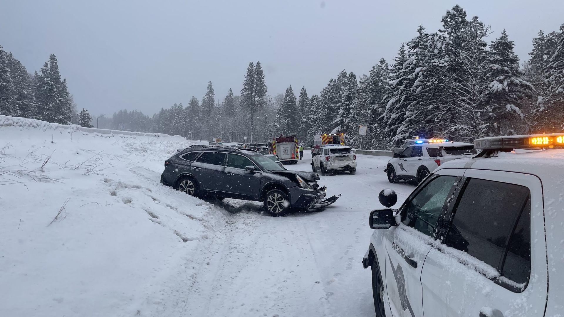 Mangled car on snowy road with emergency vehicles nearby