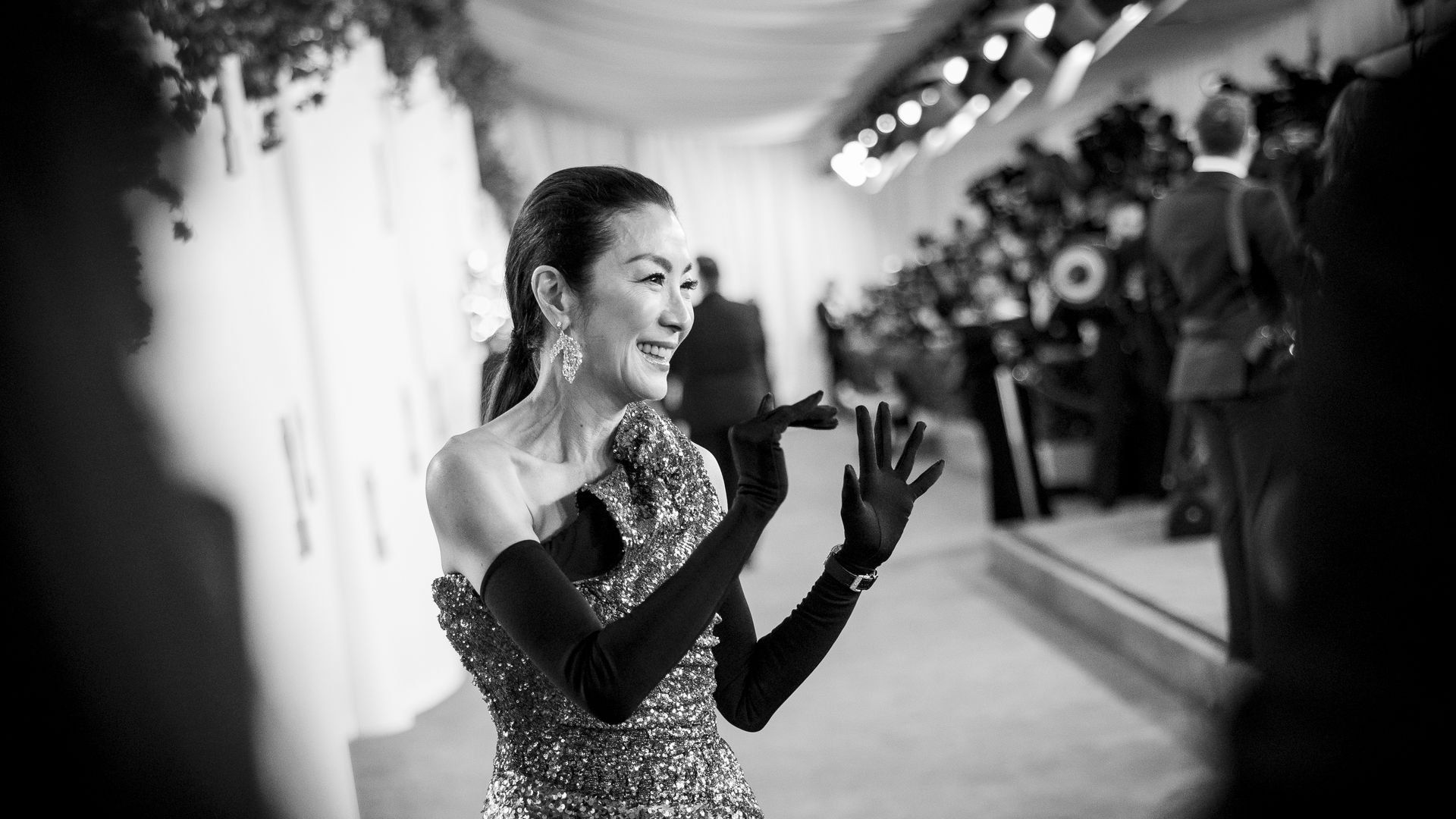 A black and white photo of Michelle Yeoh waving as she walks