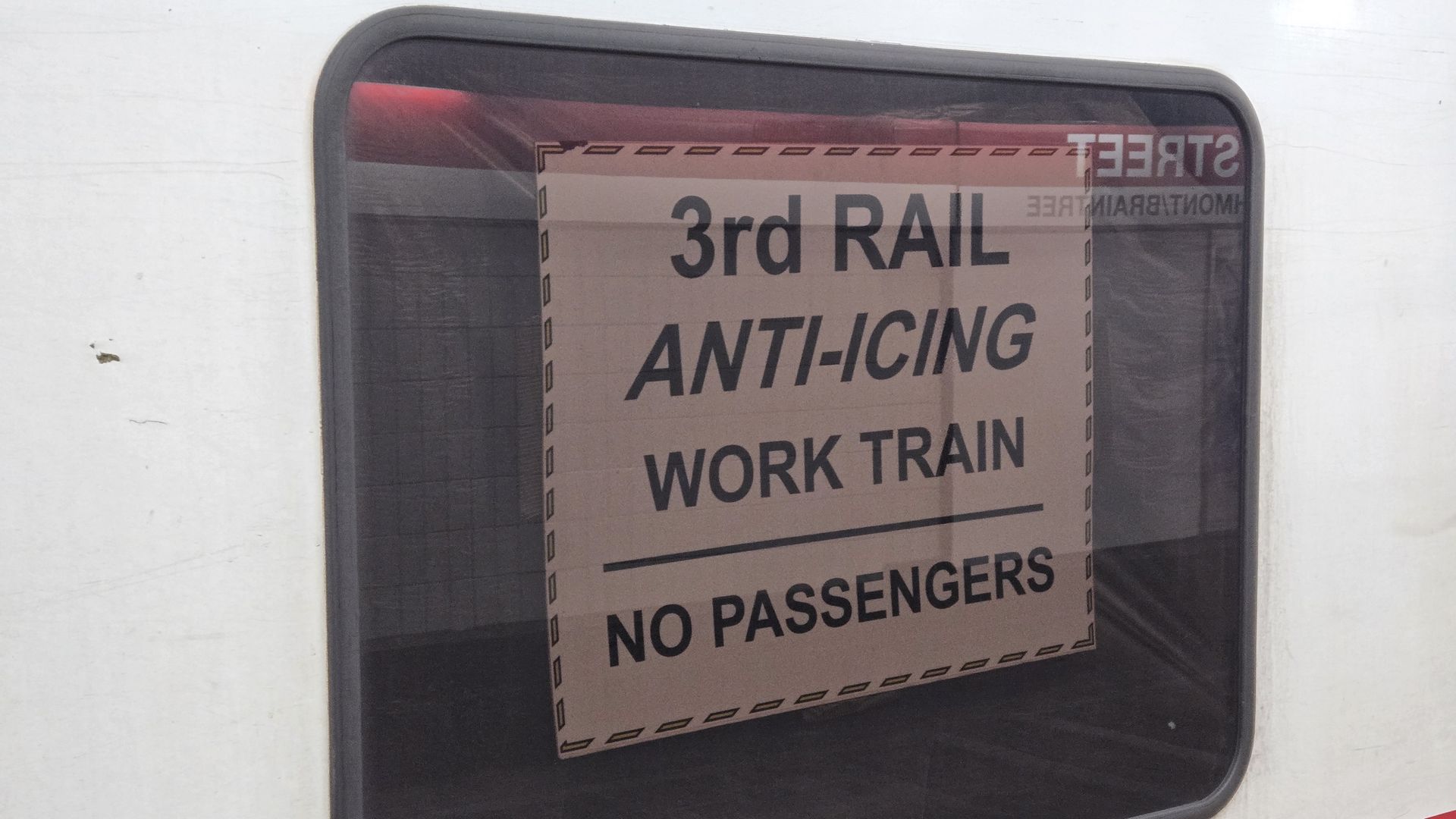 Sign inside a train window reads: "3rd RAIL ANTI-ICING WORK TRAIN NO PASSENGERS". The train exterior is white with a red stripe below the window.