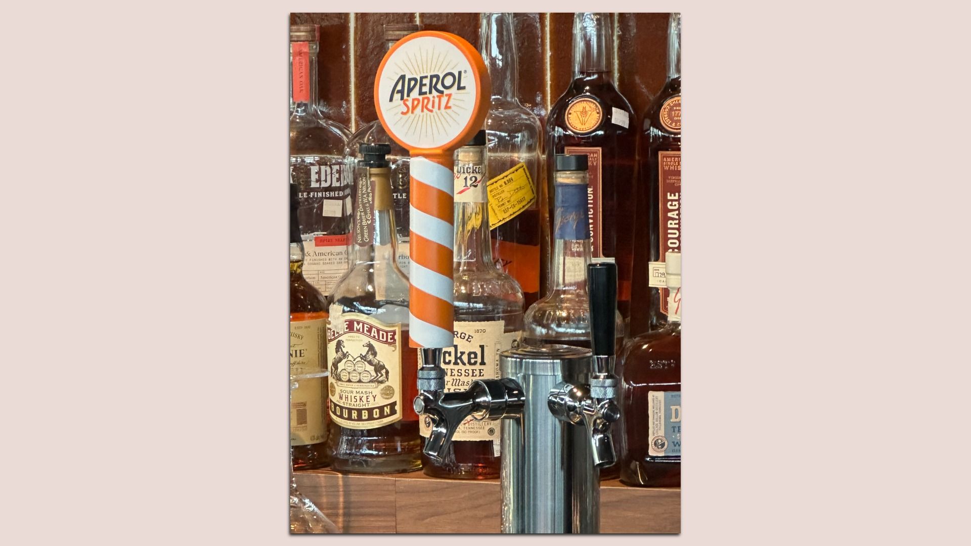 Bar display with an orange-and-white striped tap pole and a round sign reading "APEROL SPRITZ," surrounded by glass liquor bottles and vintage labels.