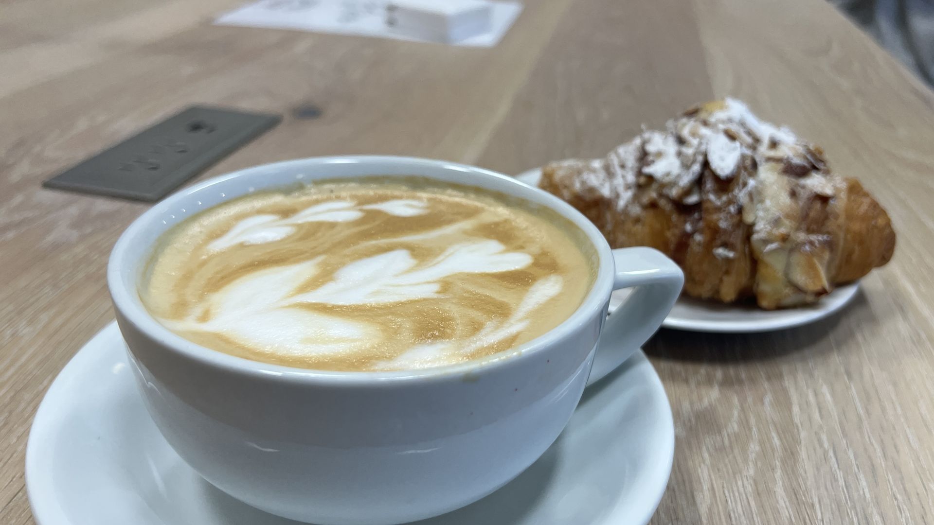 A latte in a white mug with a pastry in the background
