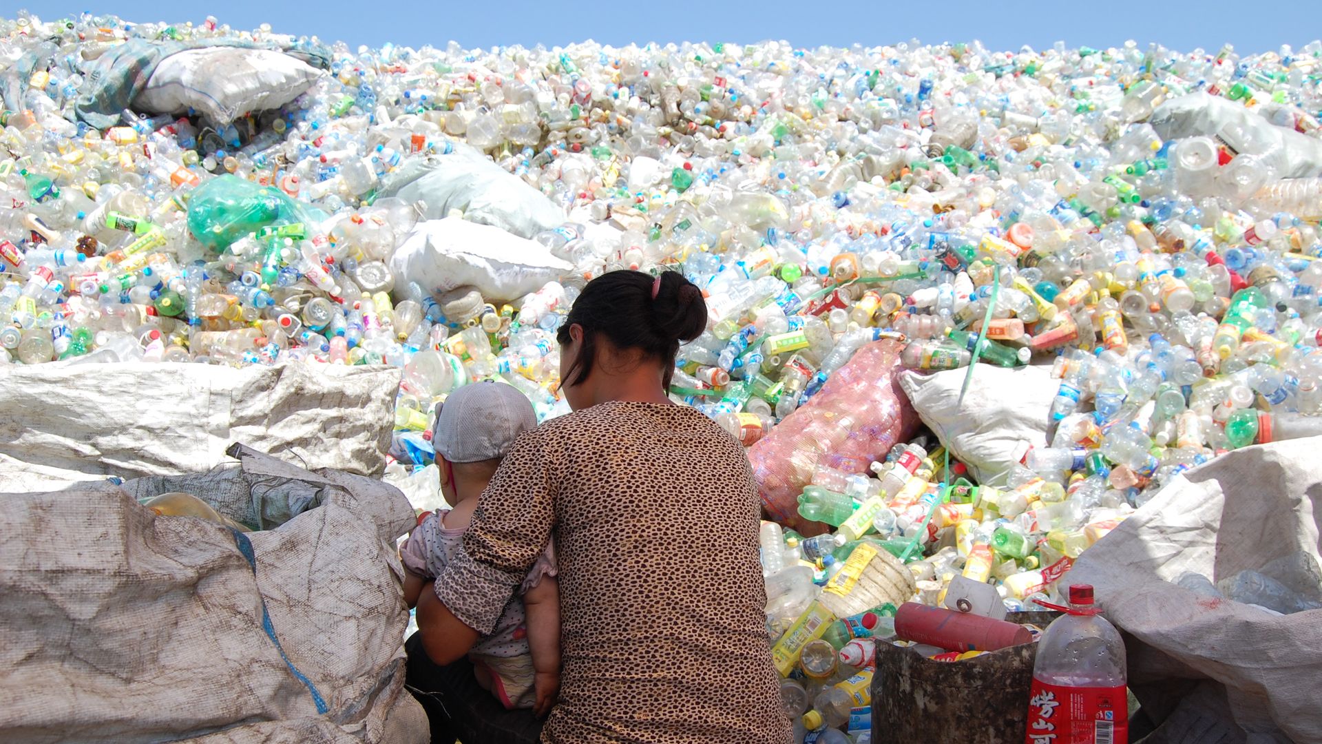 A woman sits with her baby in a sea of plastic bottles