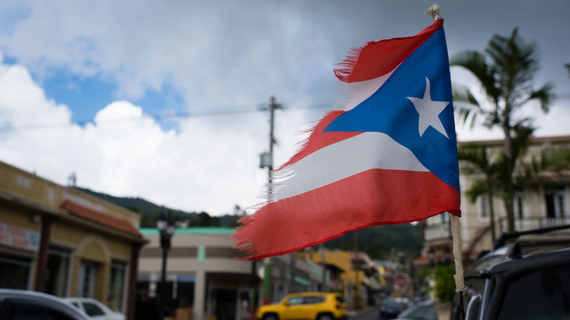 Photo of a battered Puerto Rican flag hanging from a vehicle parked in the streets