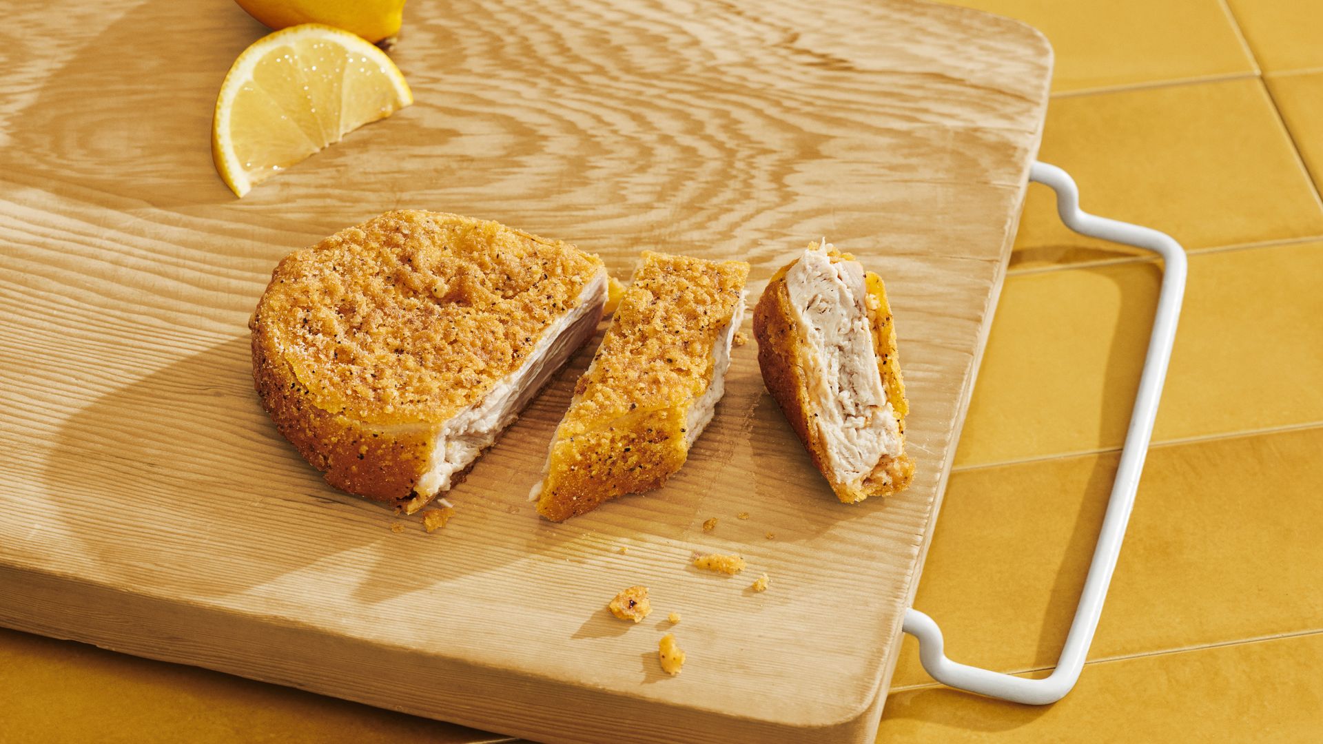 A sliced plant-based chicken cutlet is displayed on a cutting board.