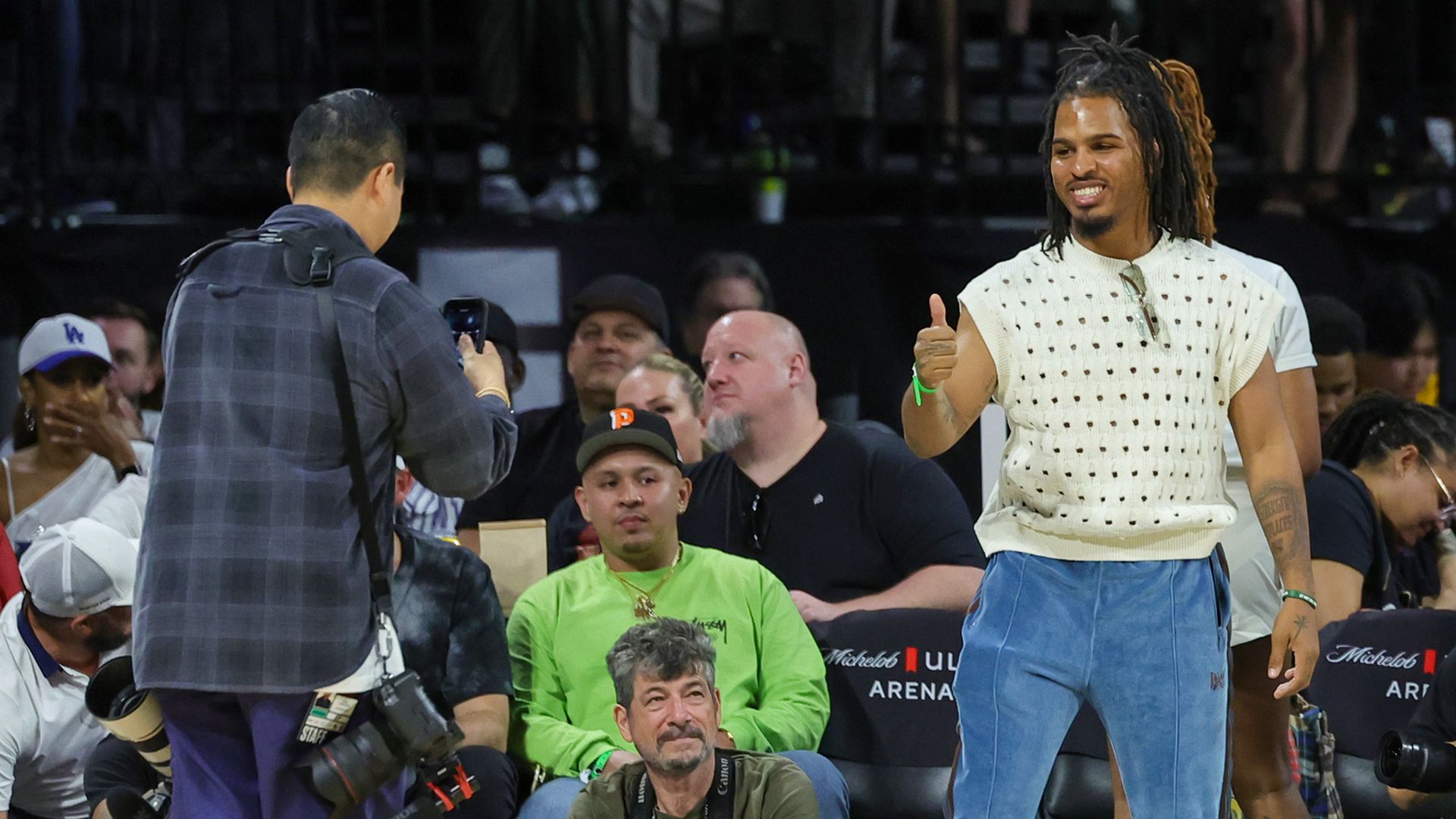 A man poses for a photo at a basketball game, with a thumbs up