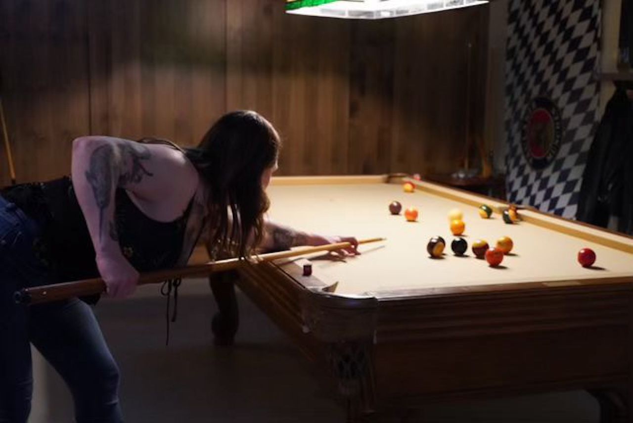 A person is playing pool on a tan felt pool table