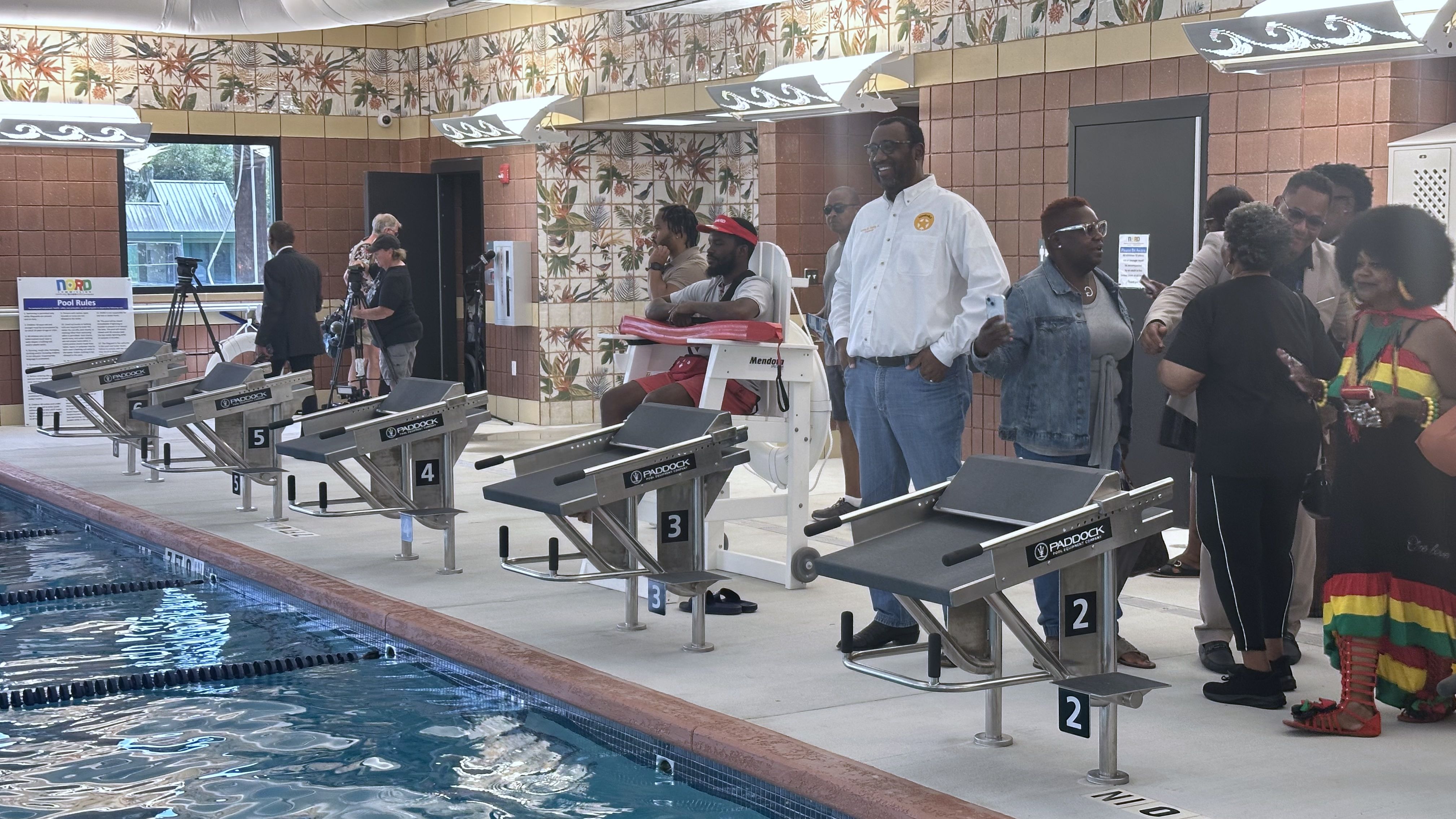 A crowd of people mill about behind a lifeguard who watches over a pool.