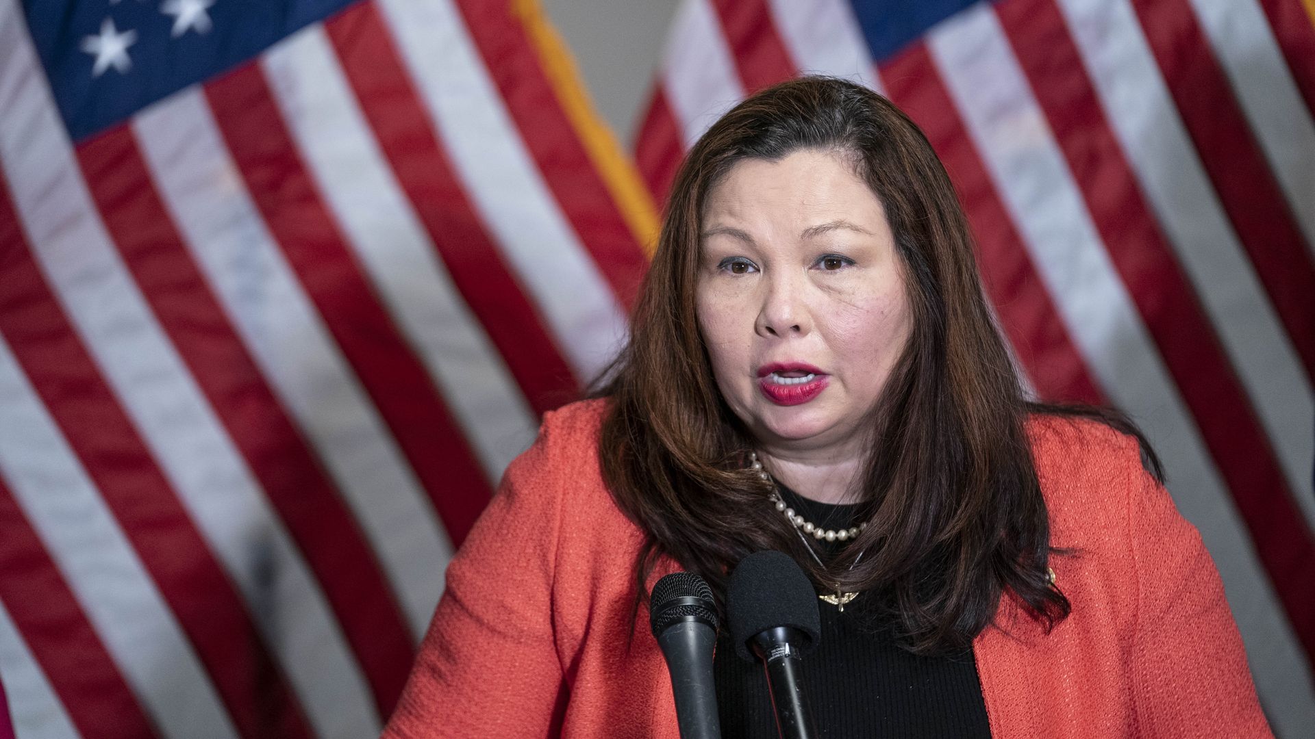 Photo of Tammy Duckworth speaking from a podium with two American flags behind her