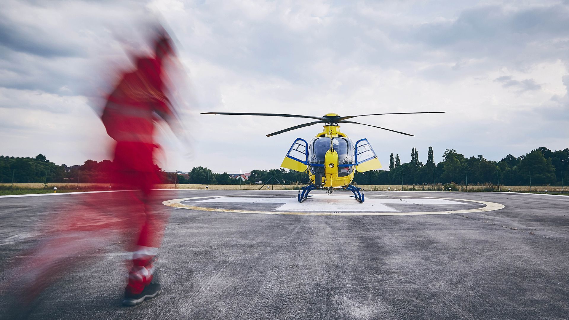 A person in a red uniform running to a yellow helicopter.