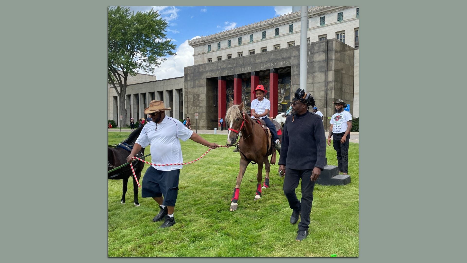 Cowboys escorting a kid on a pony in front of the library