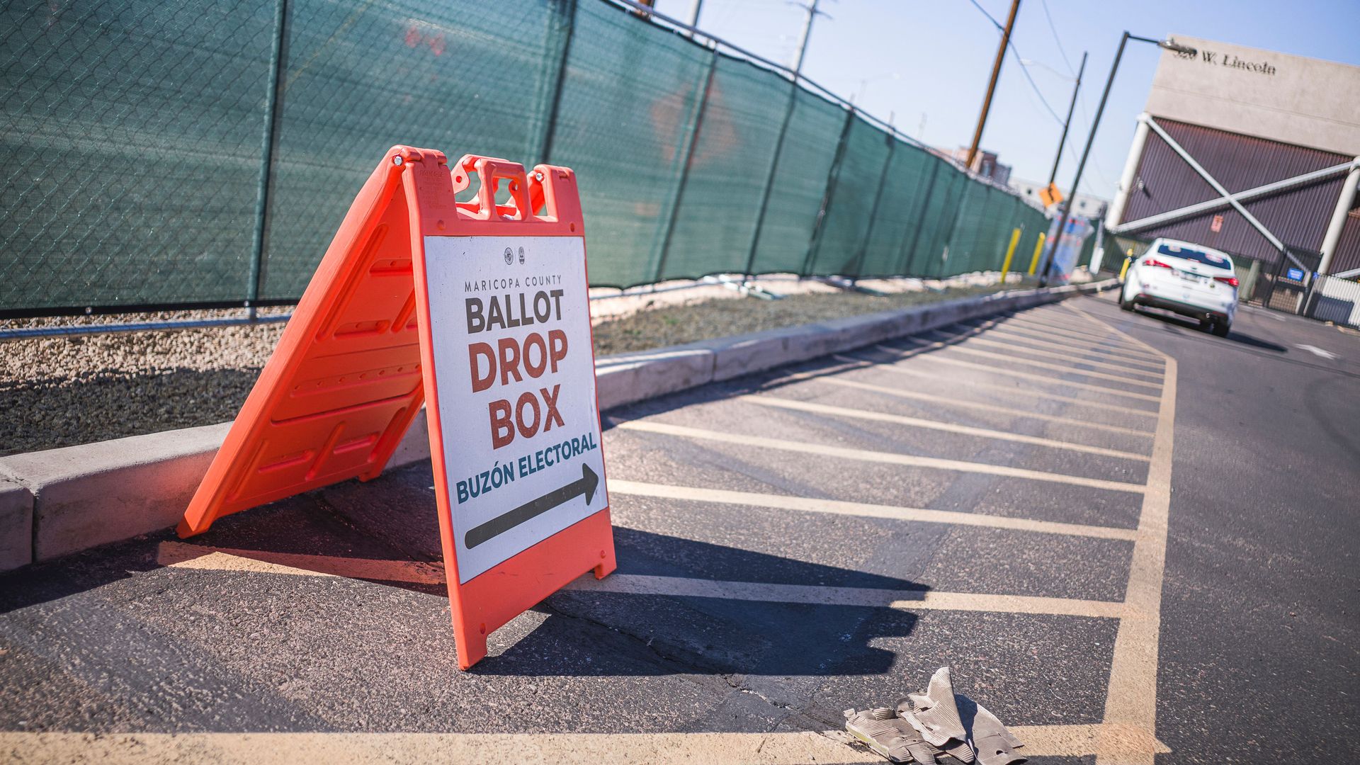Photo of a sign that shows the direction of the ballot drop box stationed in front of a fence