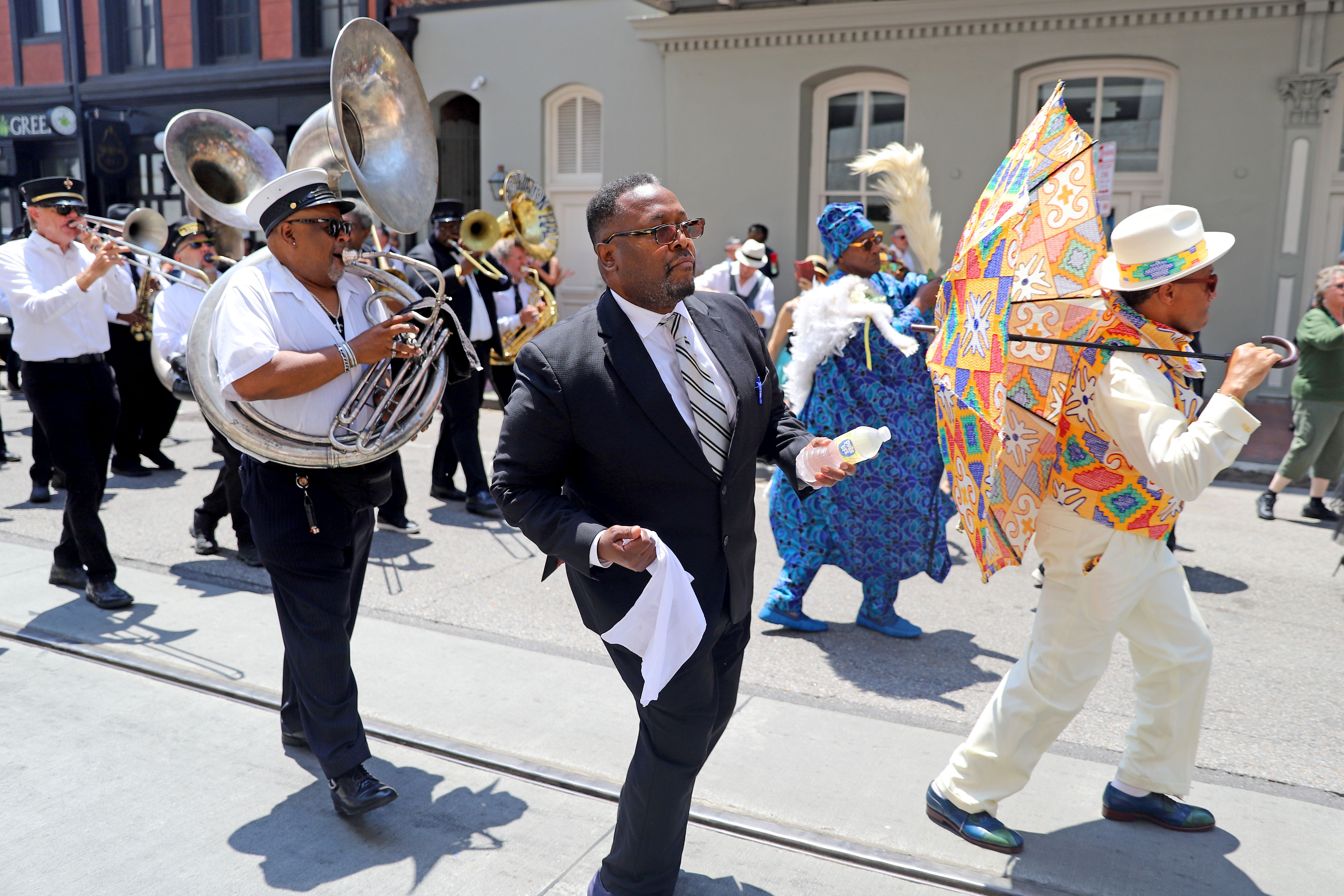 Wendell Pierce, wearing a suit, second-lines with a brass band through the French Quarter.