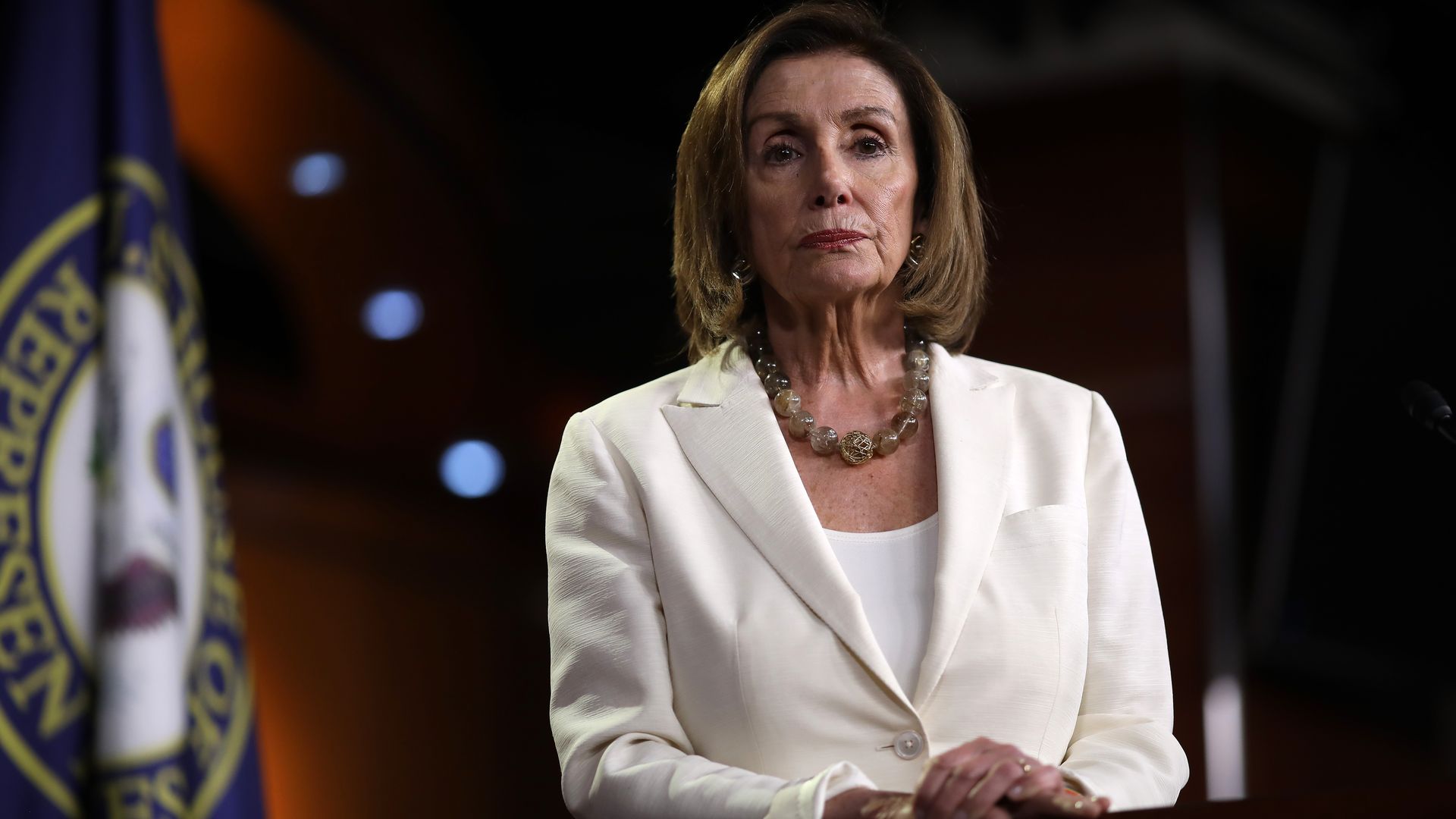 Nancy Pelosi standing up wearing a white blazer.