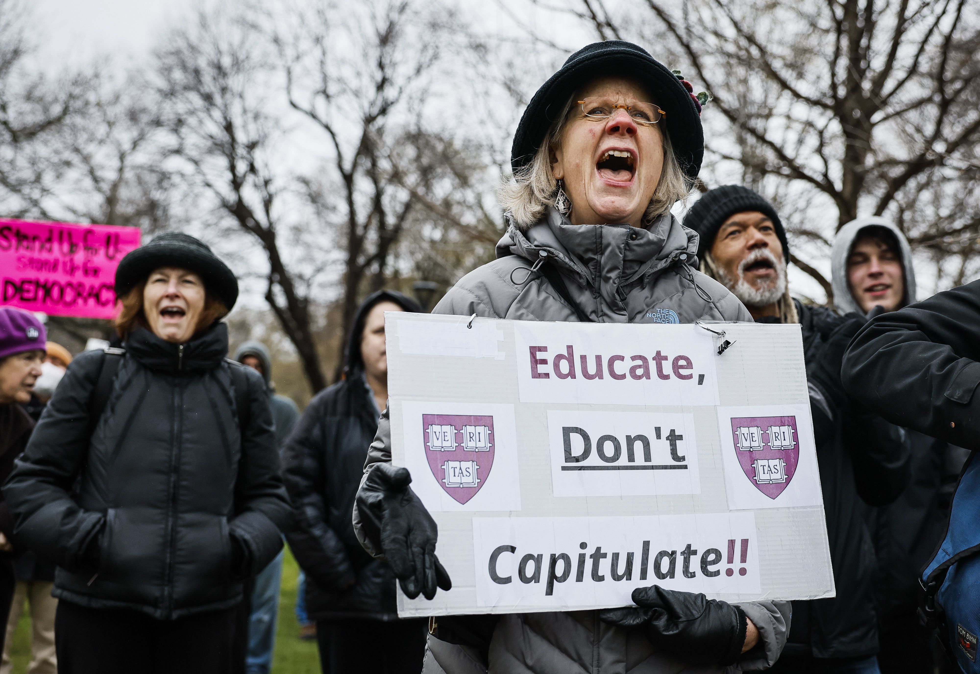A protester holds a sign reading "Educate, Don't Capitulate!!" featuring Harvard University shields during a rally at Cambridge Common. Allison Pingree, a Cambridge resident, joined hundreds demonstrating at the event partially sponsored by the Cambridge City Council to urge Harvard to resist Presid