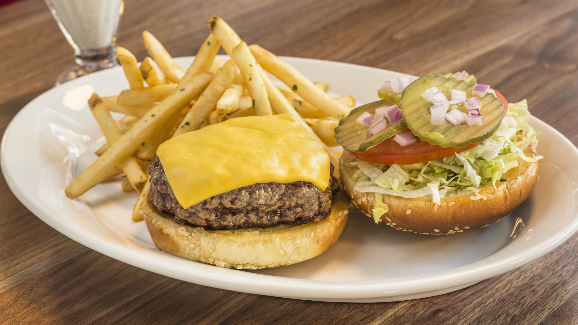 Fries and a cheeseburger on a plate with the top bun on the side, topped with veggies