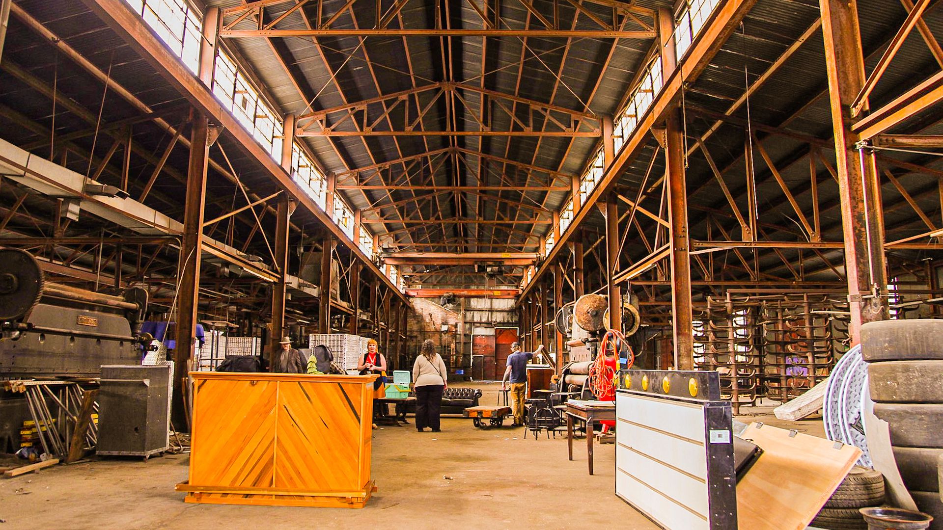 An empty manufacturing facility with clerestory windows and people celebrating the building's upcoming conversion into a kombucha brewery