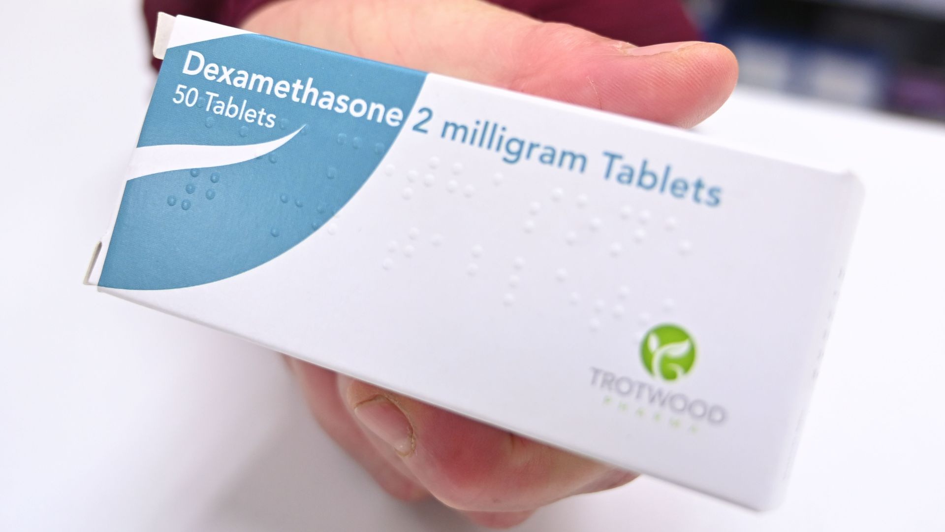 A hand holding a box of dexamethasone tablets.