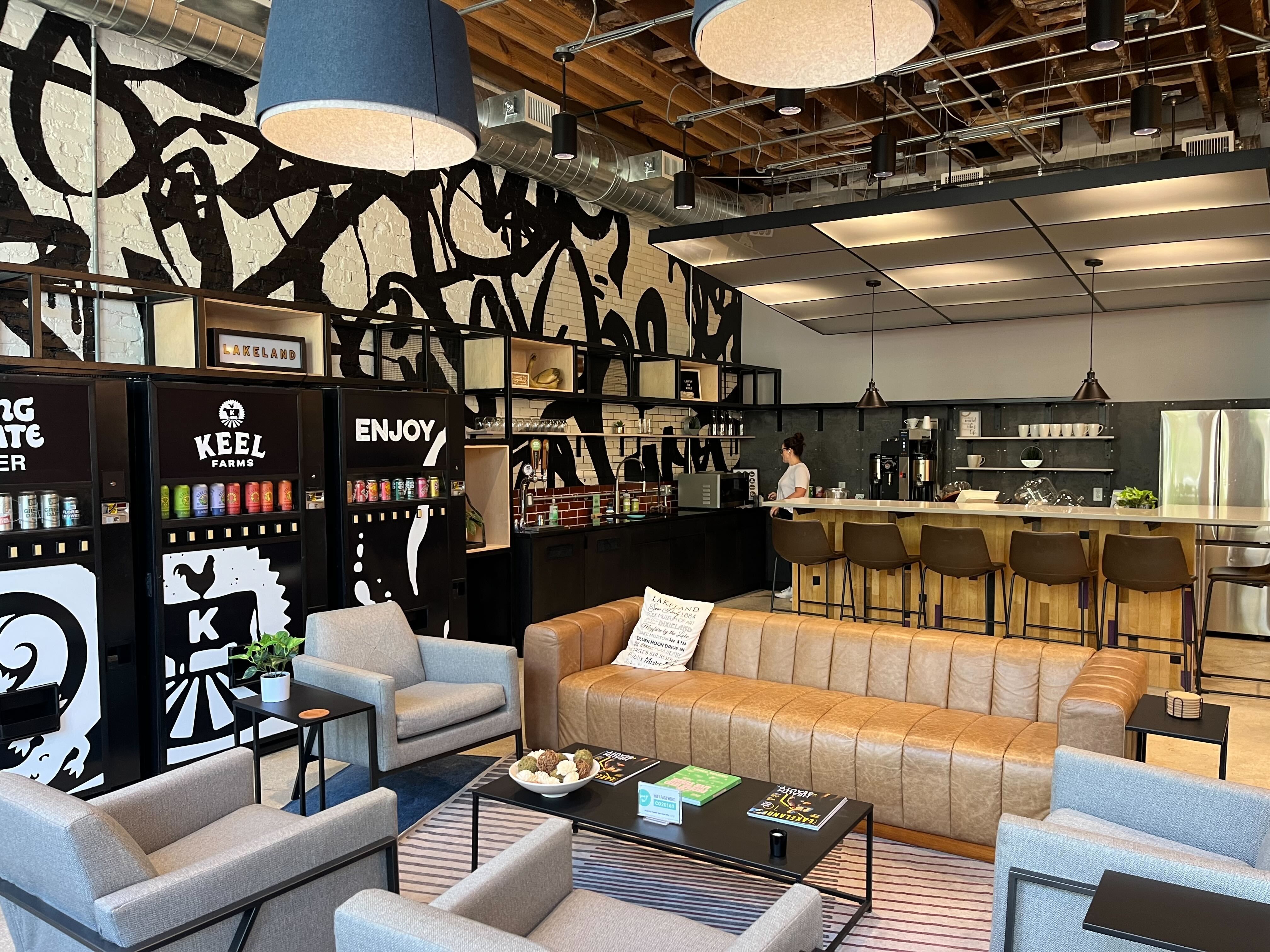 A modern interior featuring a black-and-white mural wall, a mid-century-modern style tan leather sofa and an open-plan kitchen with an island bar.